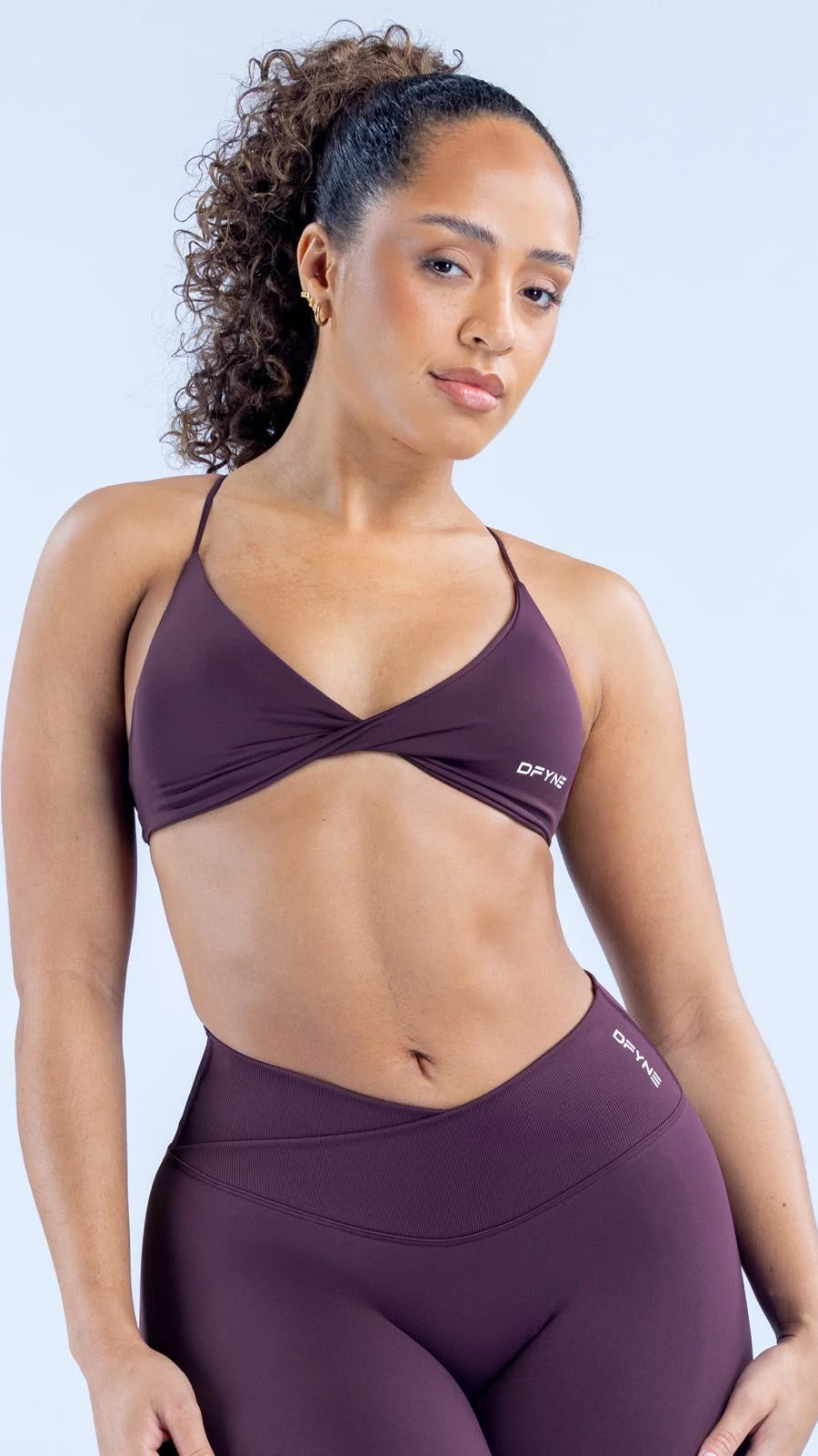 Woman wearing a maroon sports bra and leggings with a light blue background