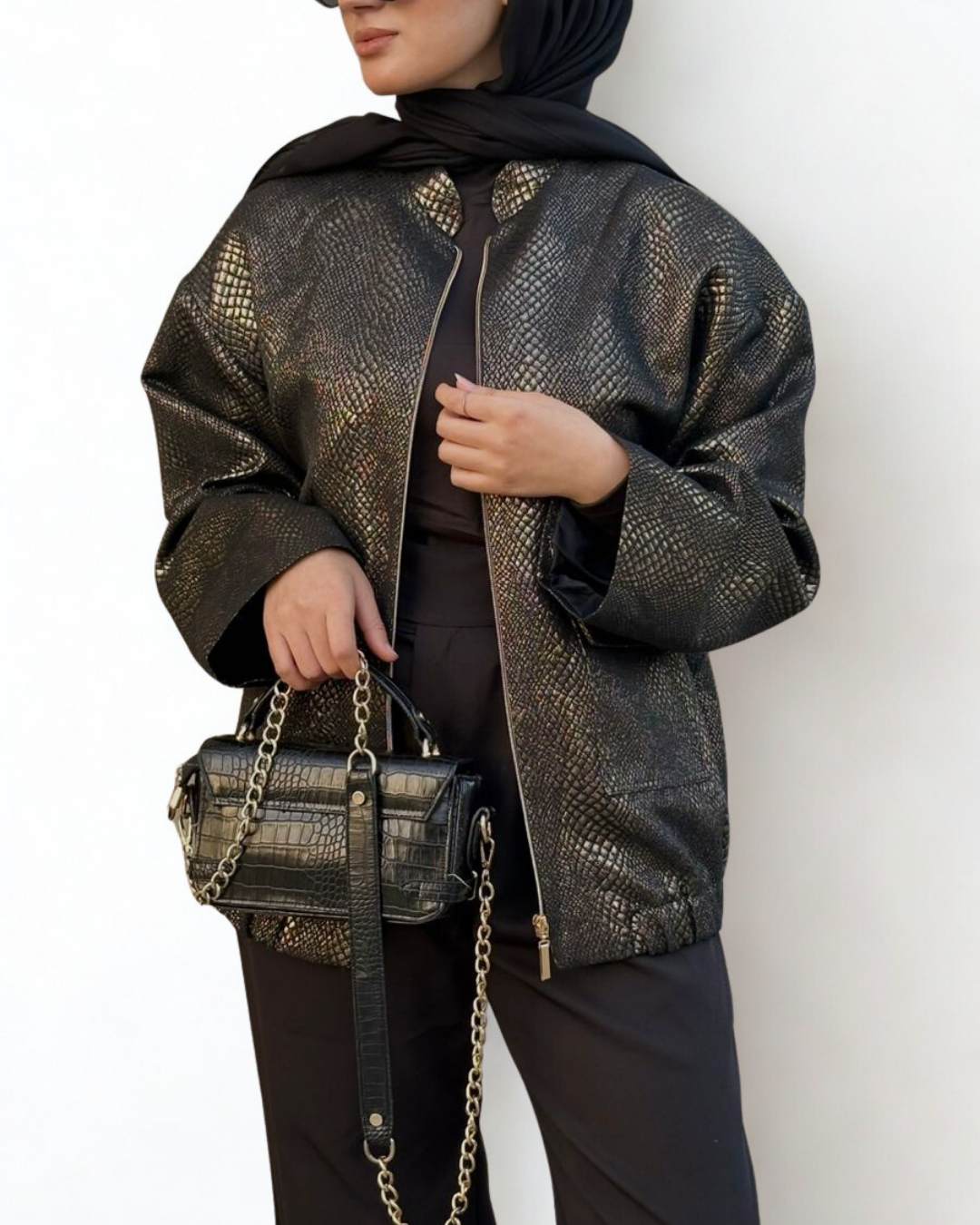 Person wearing a black textured jacket holding a matching handbag against a white background