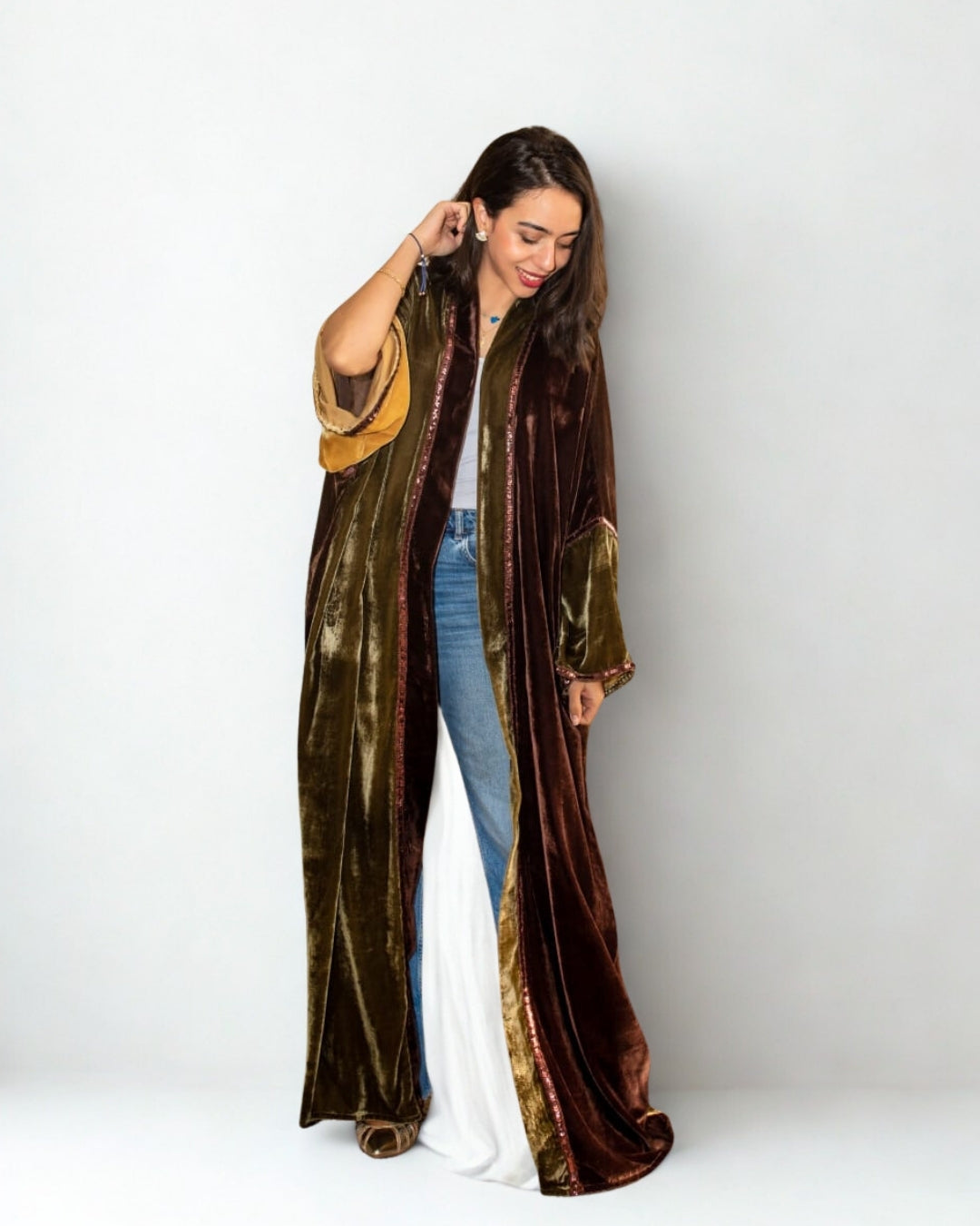 Woman wearing a long, patterned coat over a white top and blue jeans on a white background