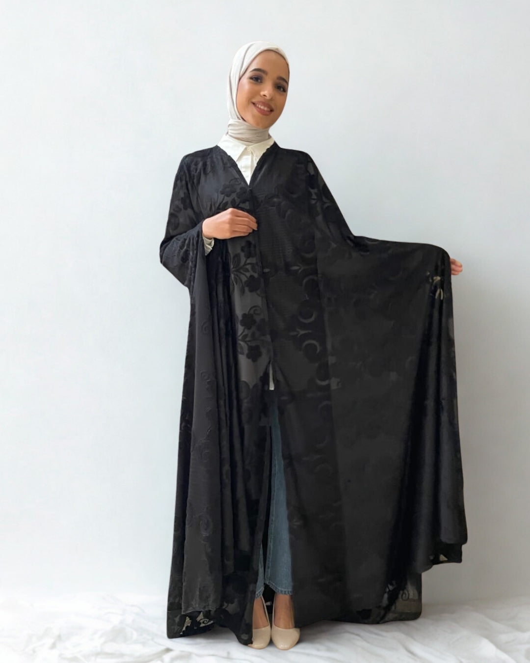 Woman holding a black abaya with floral patterns on a white background