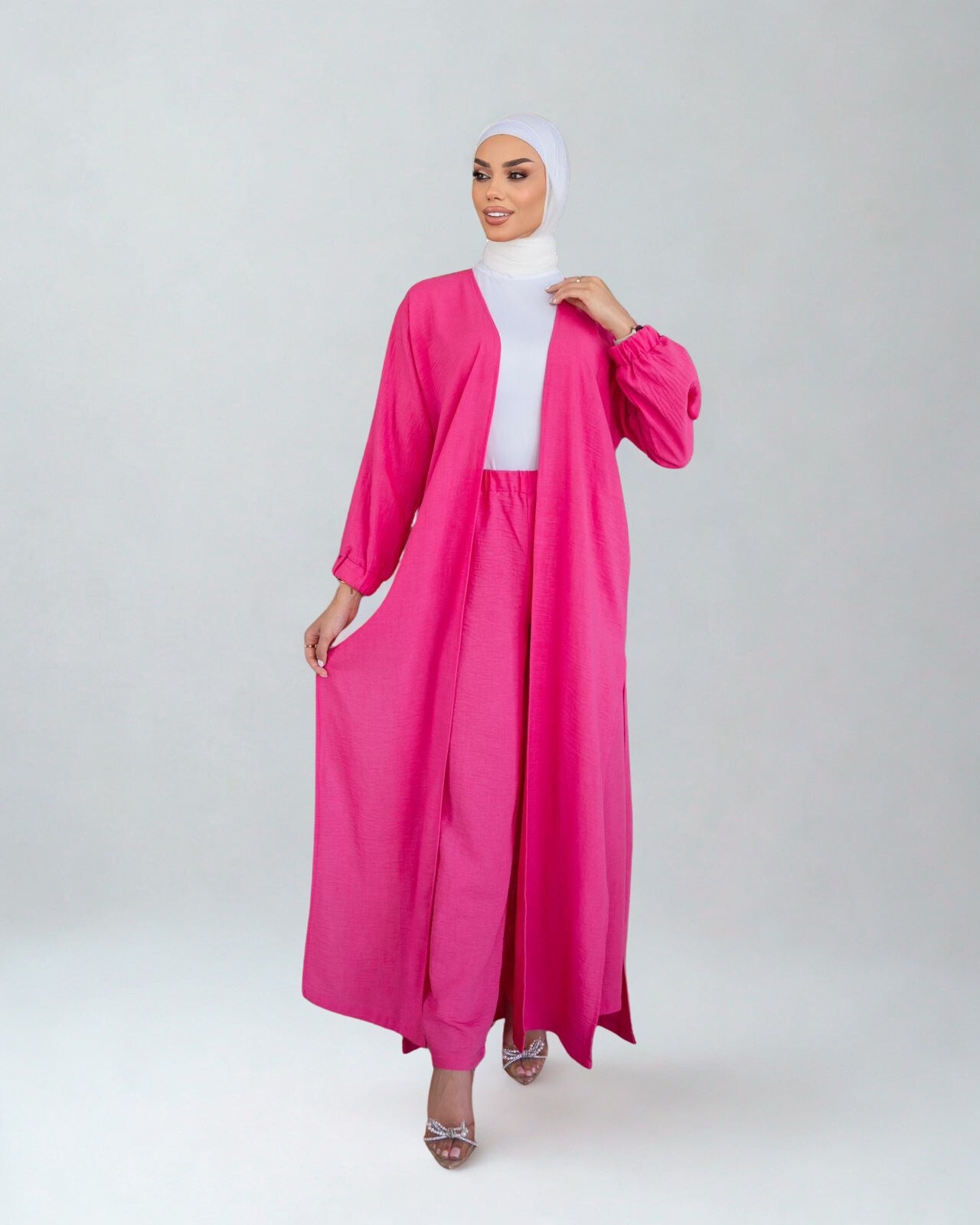 Woman wearing a bright pink abaya with a white hijab on a white background