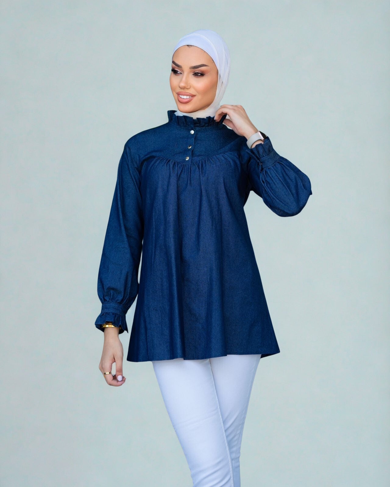 Woman wearing a blue blouse and white hijab on a plain background