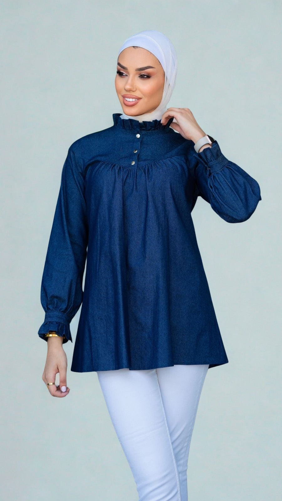 Woman wearing a blue blouse and white hijab on a plain background