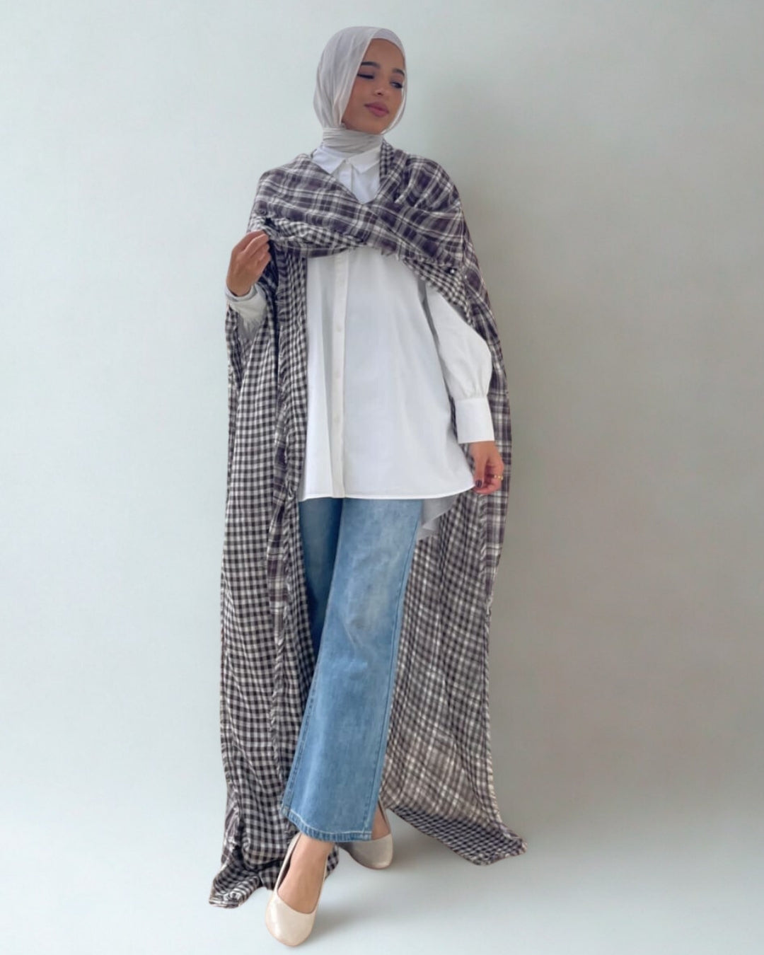 Person wearing a long plaid scarf, white shirt, and blue jeans on a plain background