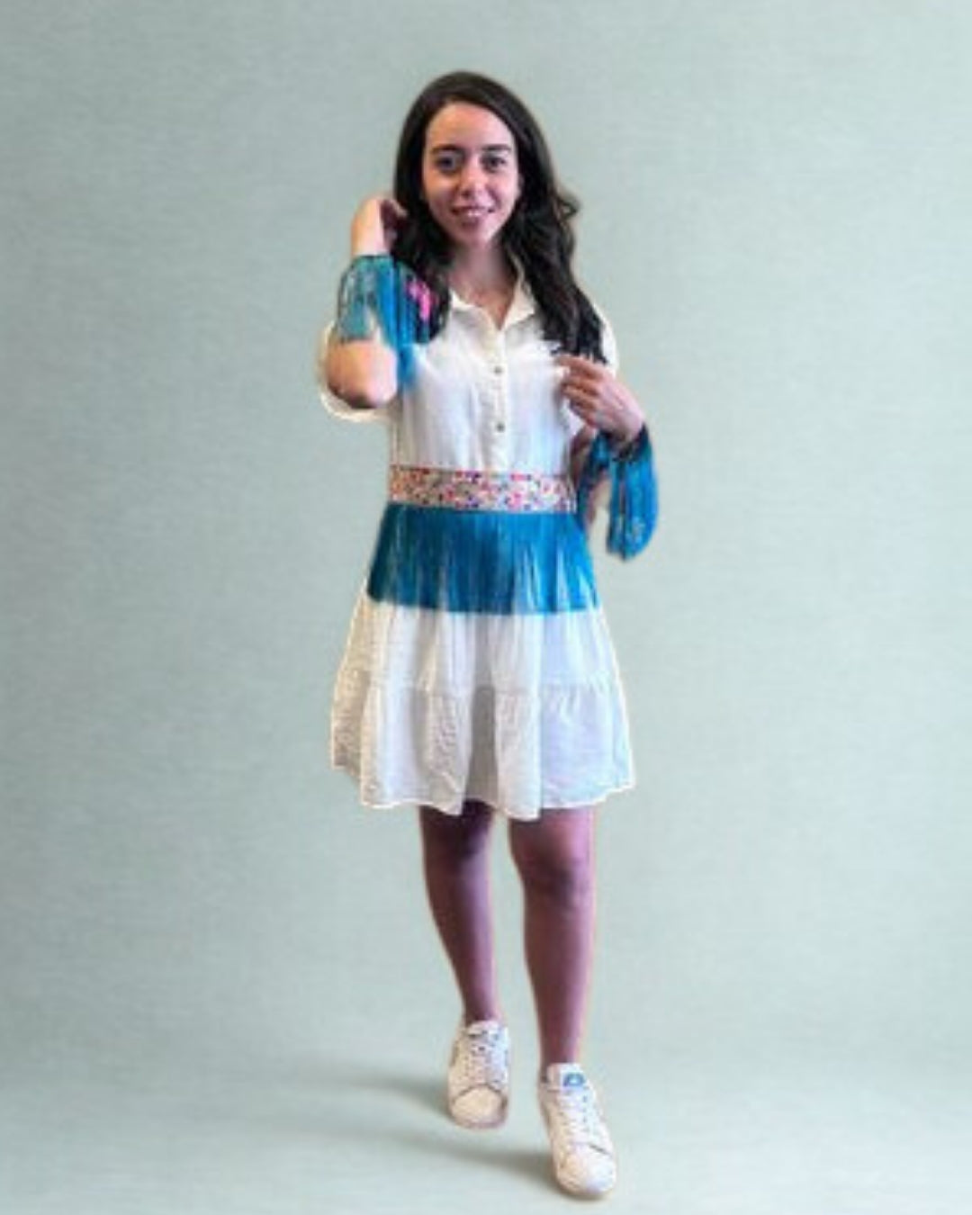 Woman wearing a white dress with blue accents and floral details on a plain background