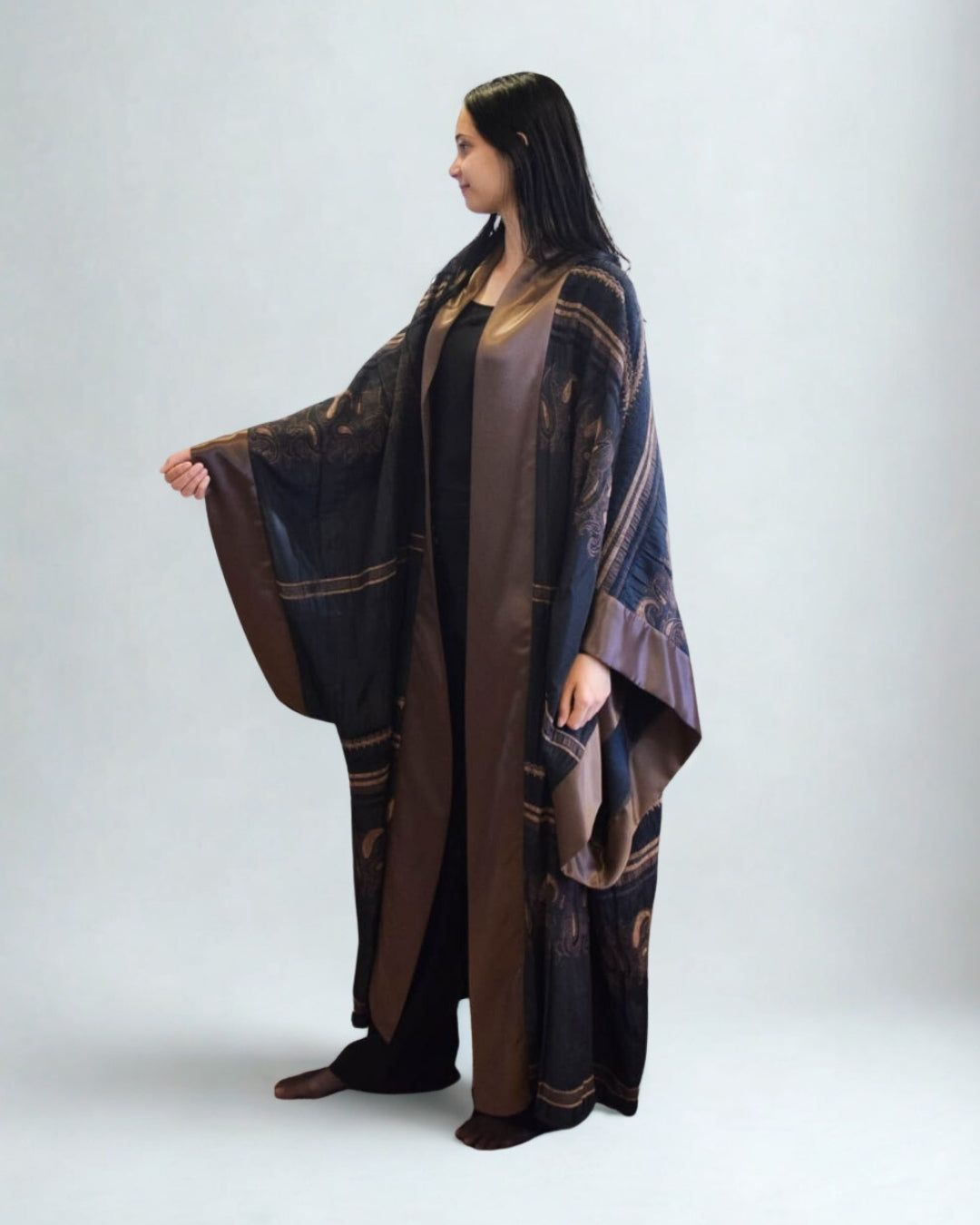 Woman wearing a long, dark-colored dress with gold patterns on a white background