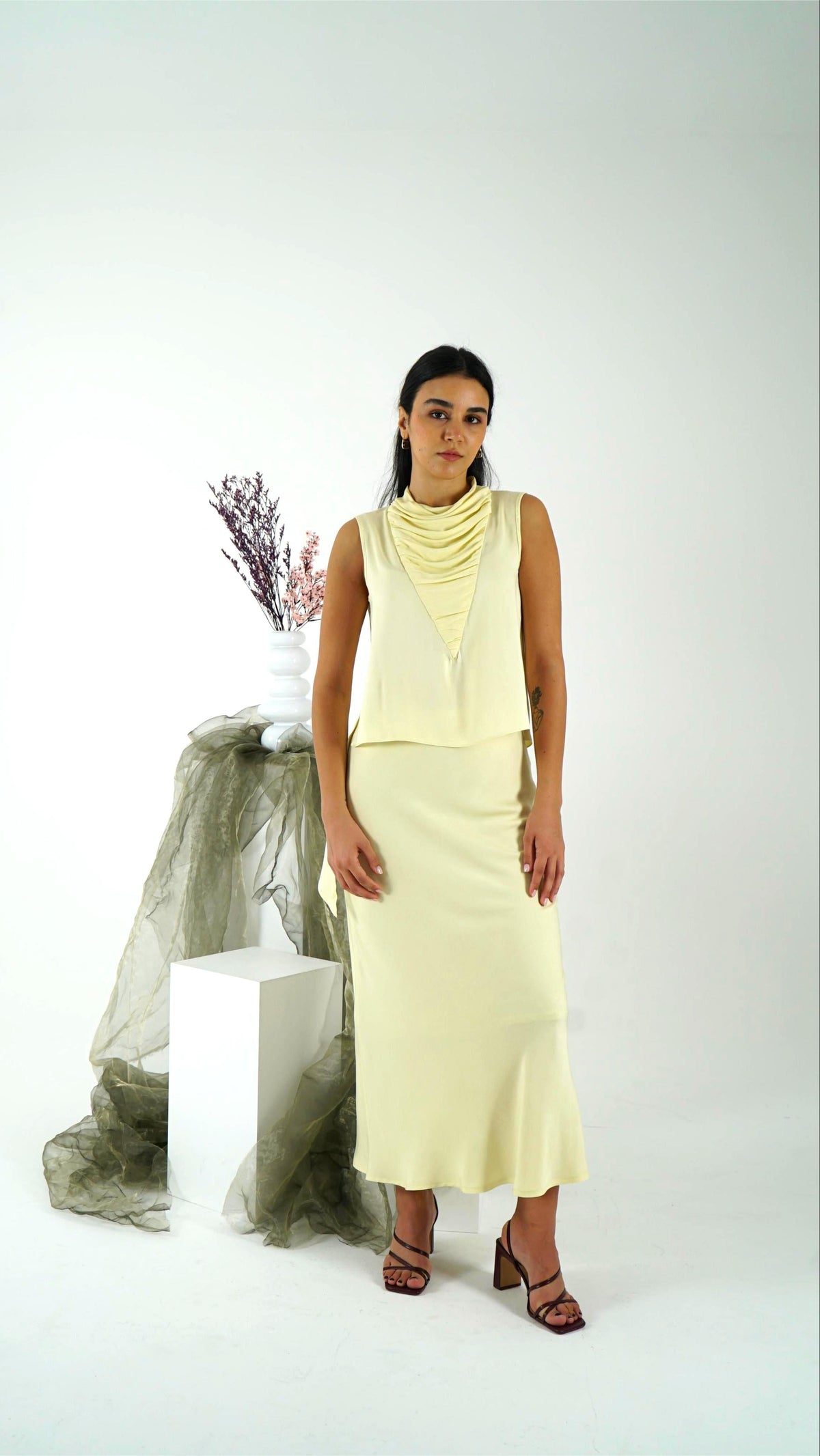Woman wearing a light yellow sleeveless top and skirt with a white background