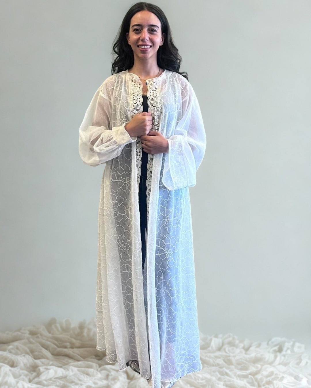 Woman wearing a long, light-colored dress with a patterned design on a white background