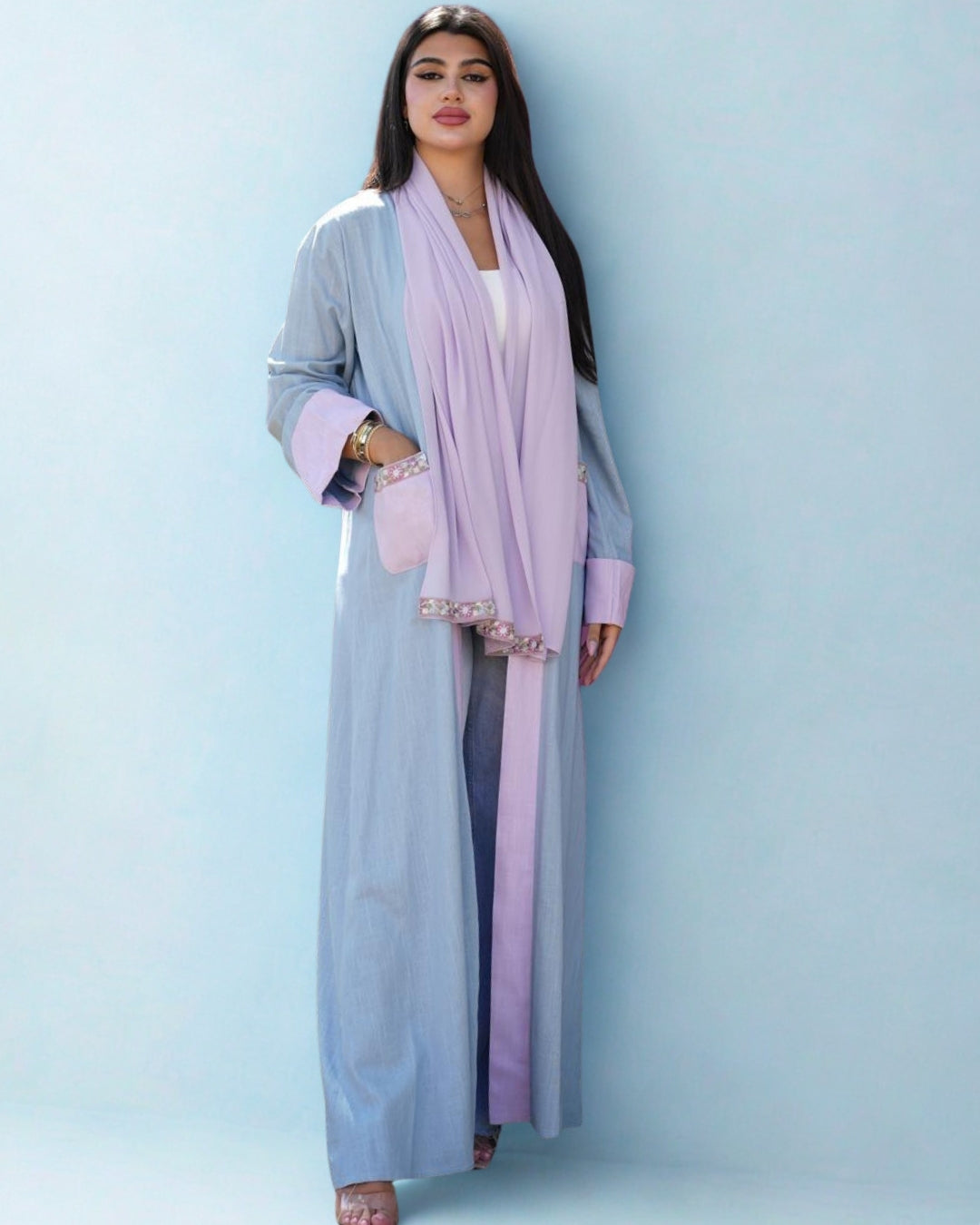 Woman wearing a light blue abaya with a pink scarf against a light blue background