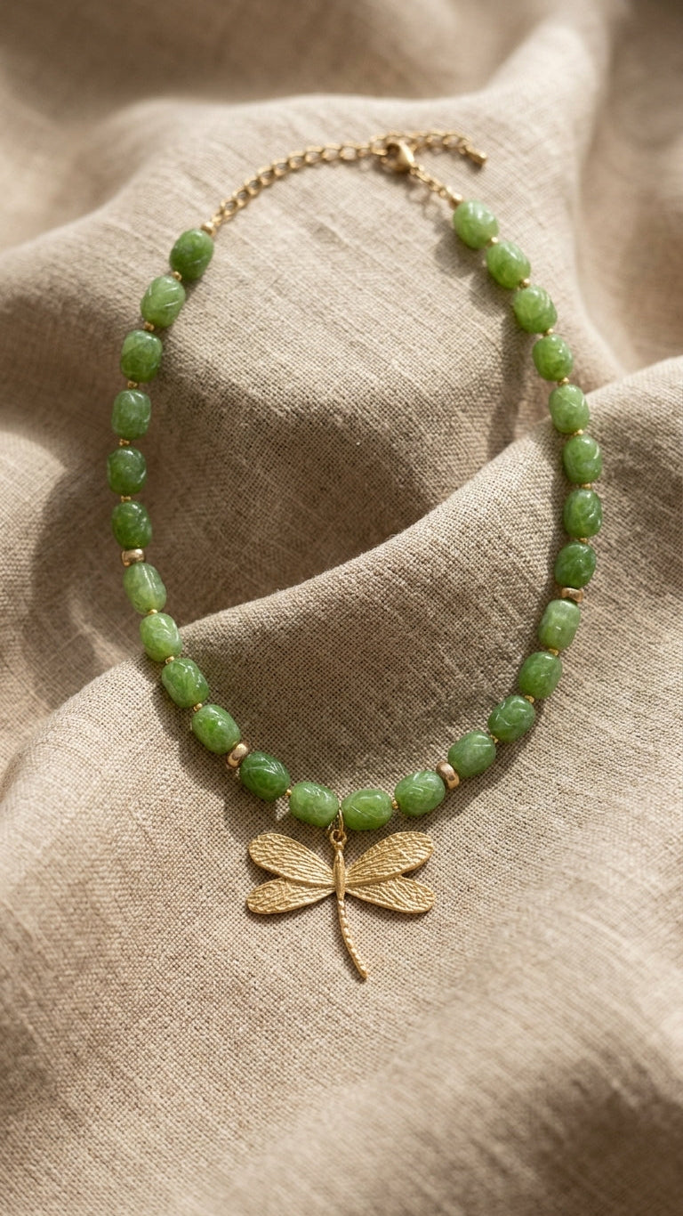 Green beaded necklace with a gold dragonfly pendant on beige fabric