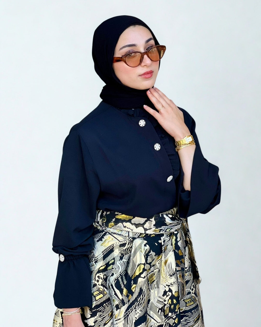 Woman wearing a dark blue blouse with white buttons and a patterned skirt on a white background