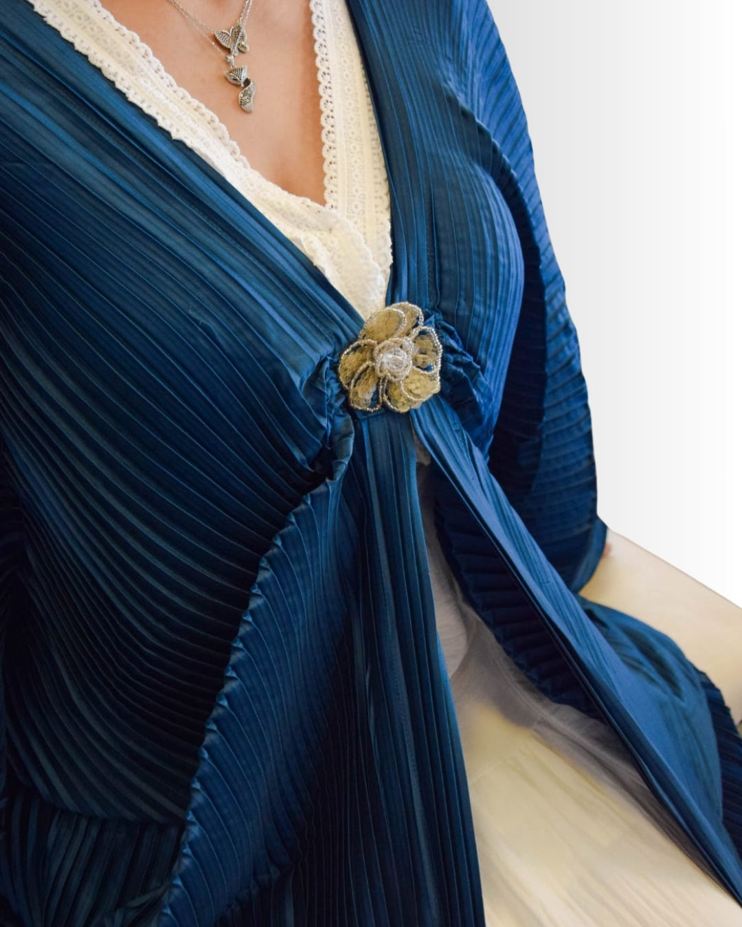 Close-up of a blue pleated garment with a decorative brooch on a white background