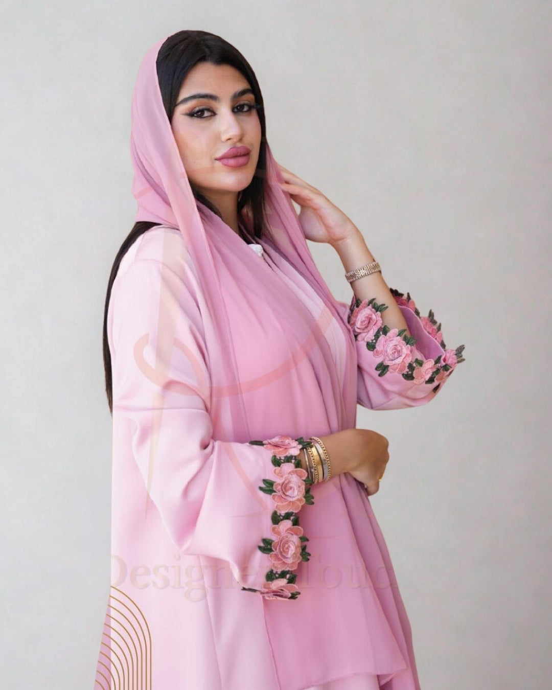 Woman wearing a pink traditional outfit with floral embroidery on a plain background