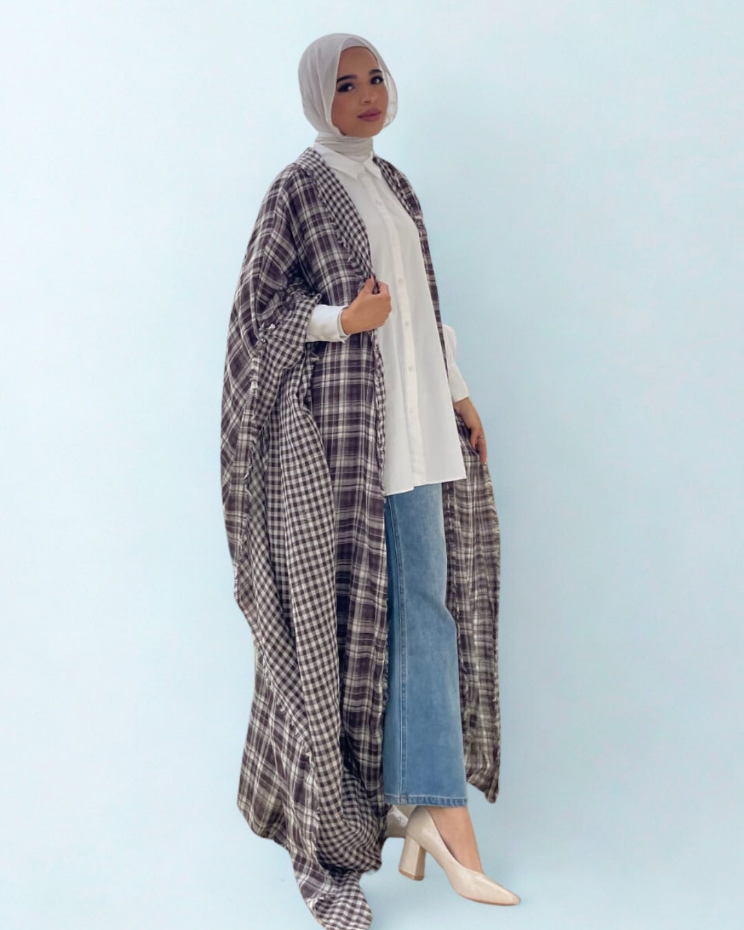 Woman wearing a plaid coat, white shirt, and blue jeans on a light blue background