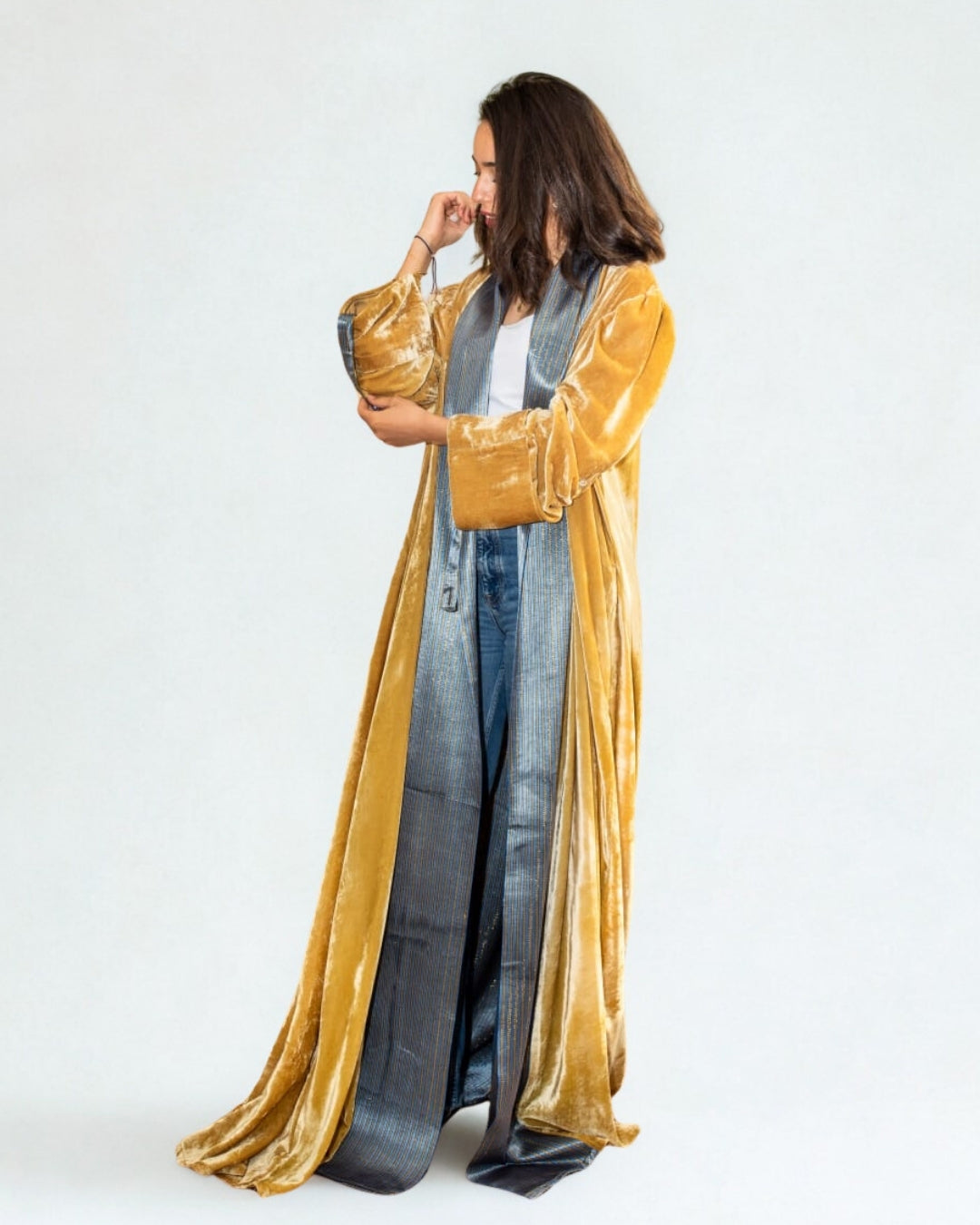 Woman wearing a long, gold robe over a denim outfit on a white background