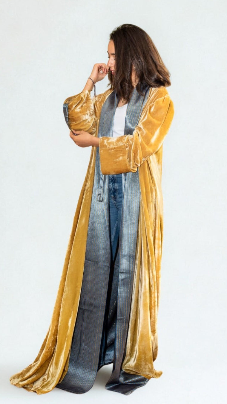 Woman wearing a long, gold robe over a denim outfit on a white background