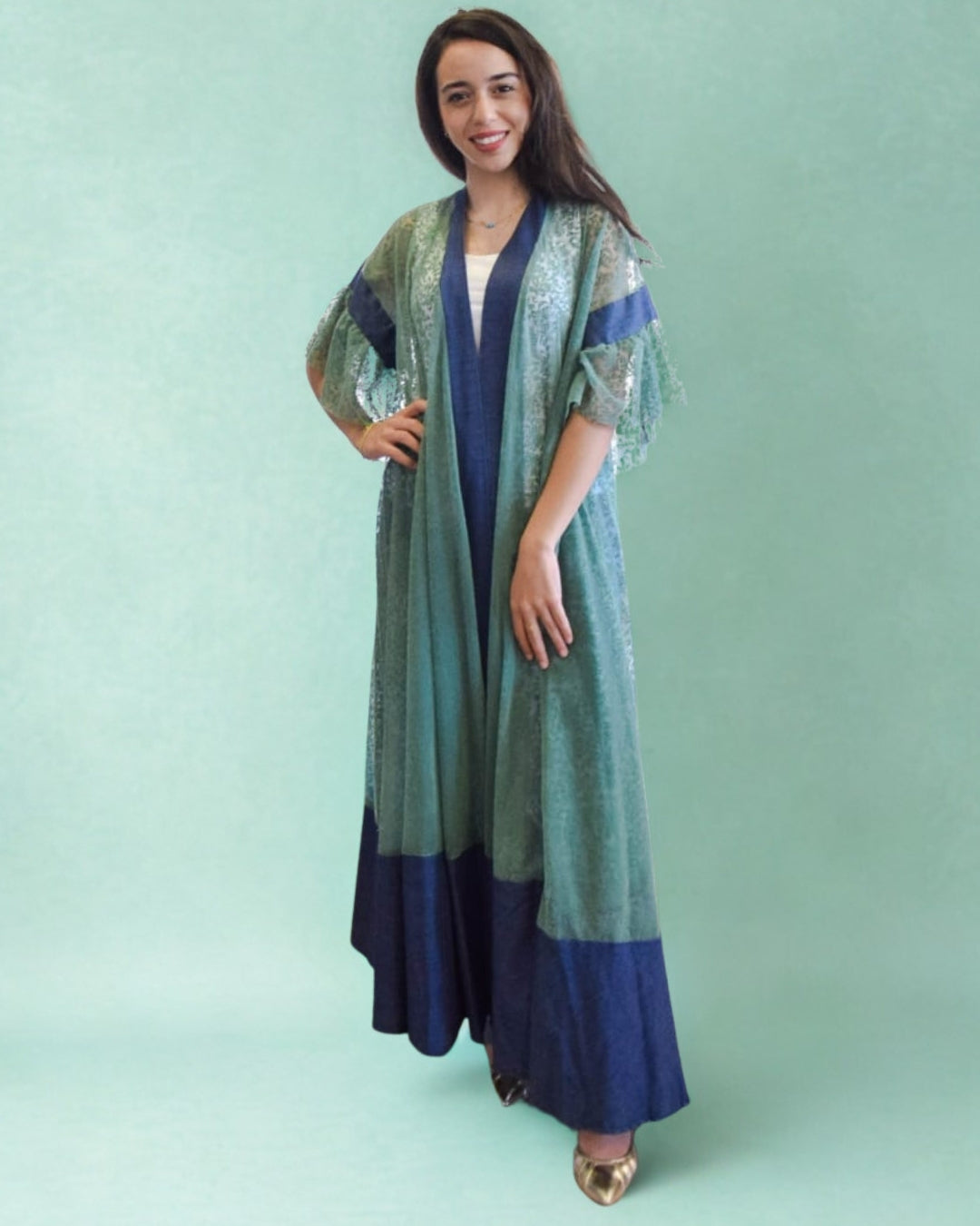 Woman wearing a long, patterned dress with a green and blue color scheme on a light green background.