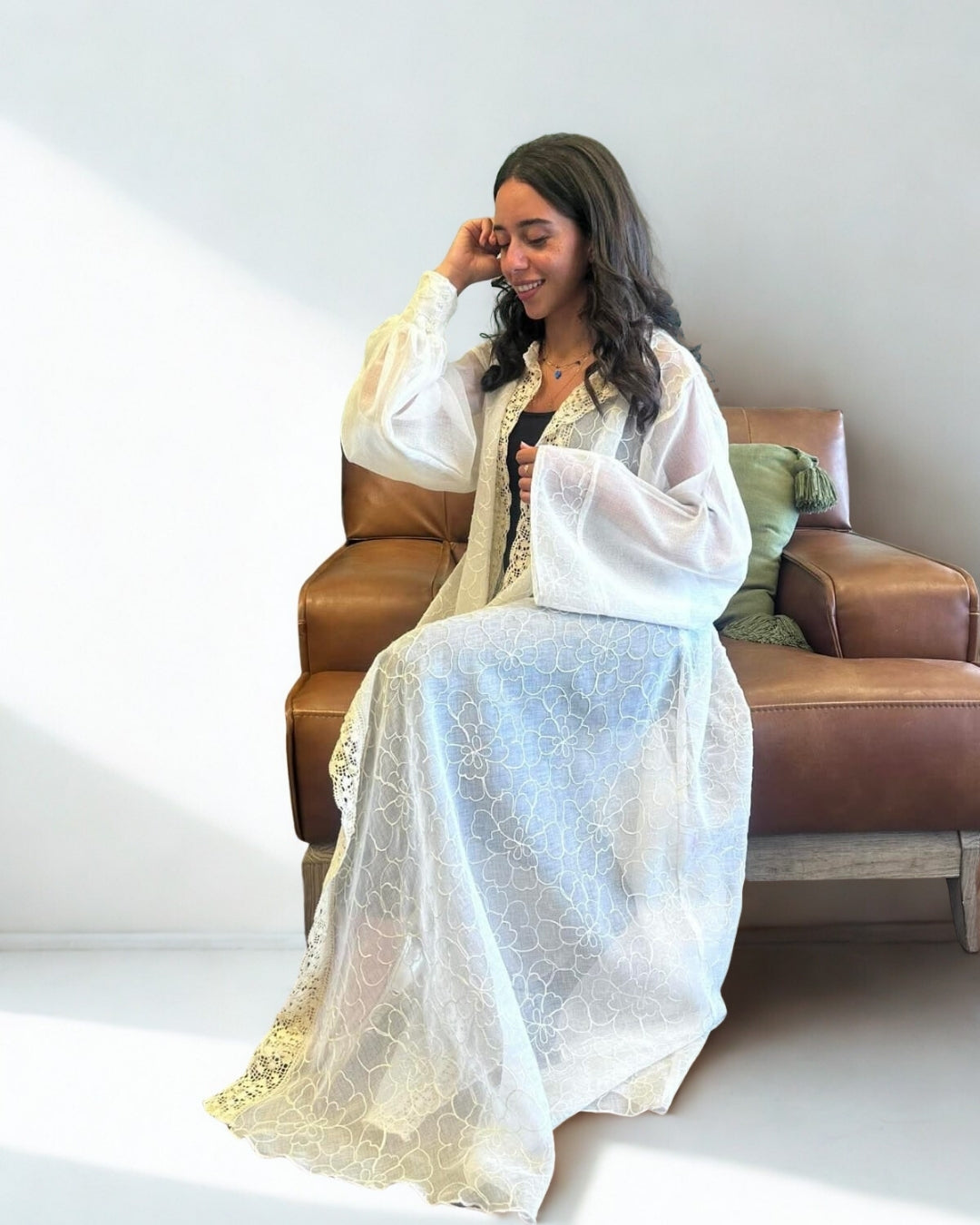Woman sitting on a brown couch wearing a white lace dress.