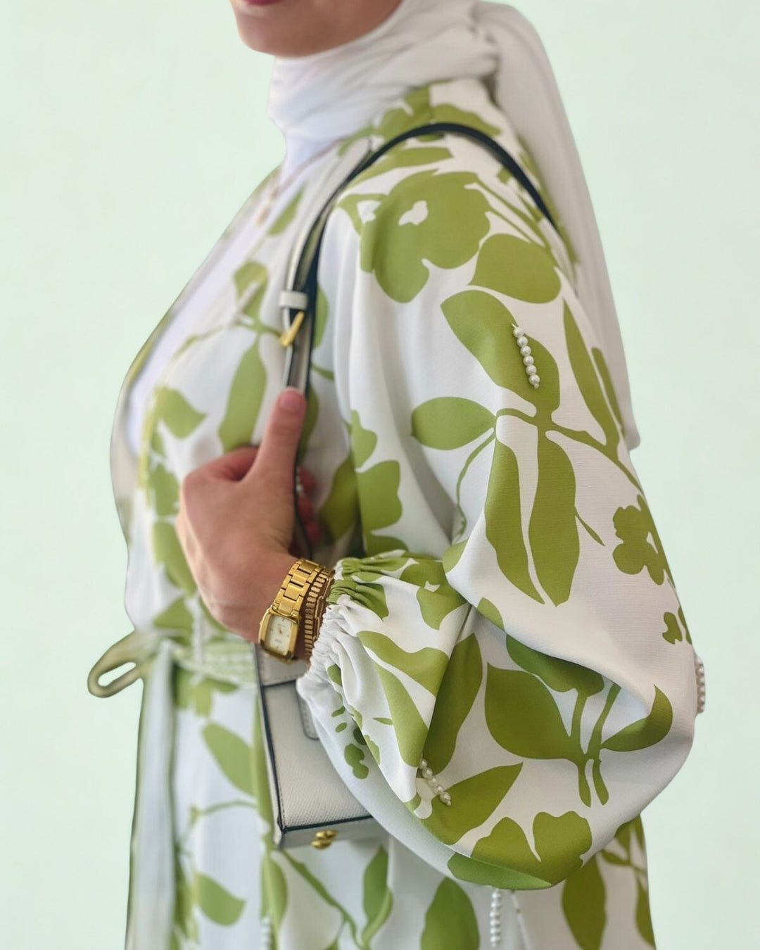 Person wearing a white outfit with green floral patterns, holding a matching handbag against a light green background.