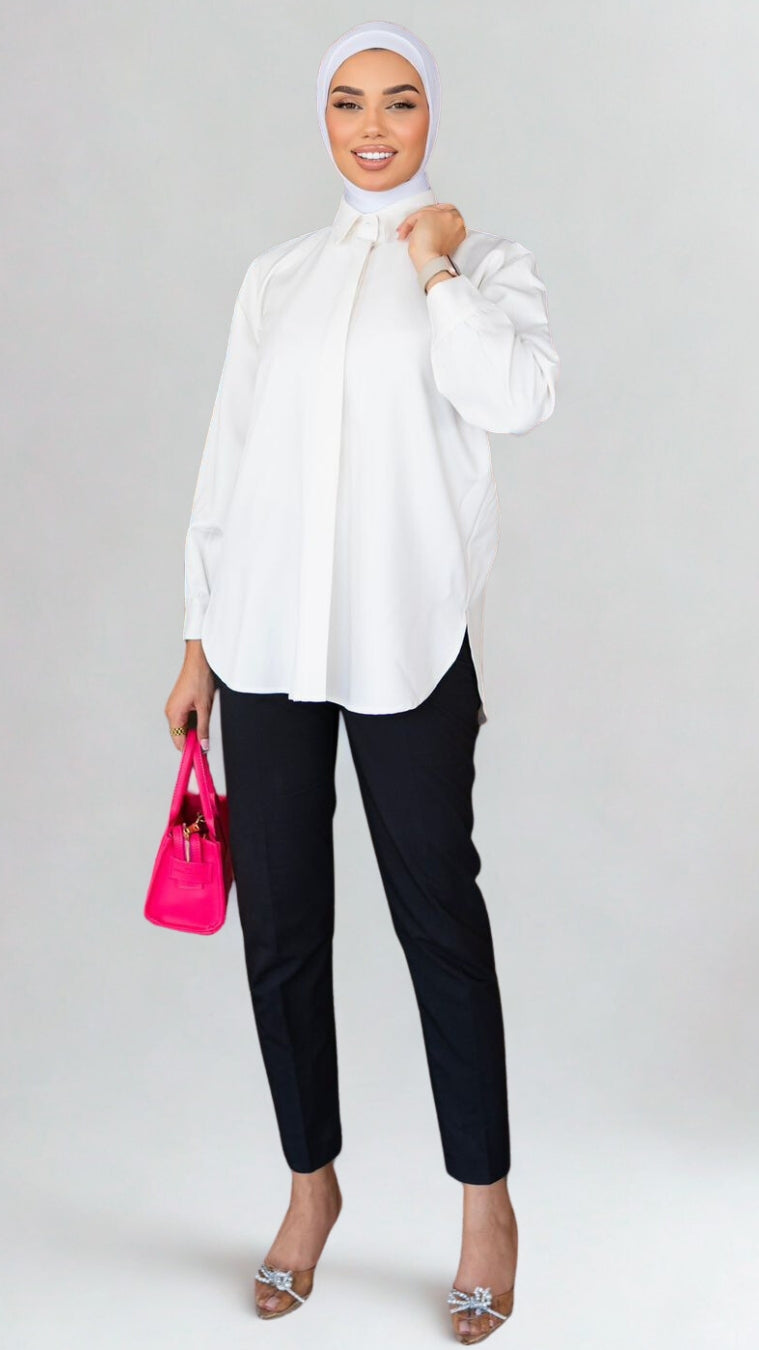 Woman wearing a white blouse, black pants, and a hijab, holding a pink handbag on a white background