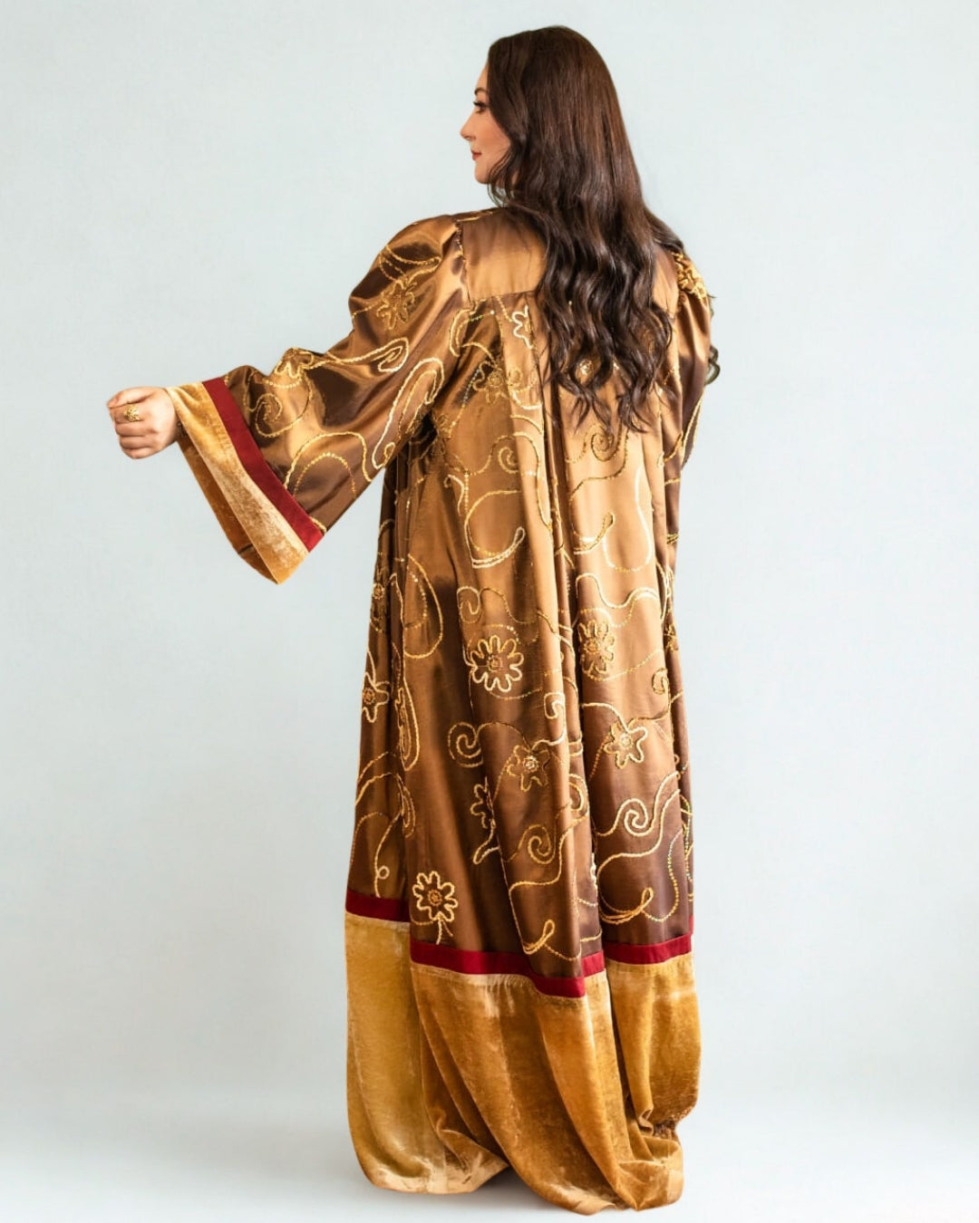 Woman wearing a long, patterned gold dress against a white background