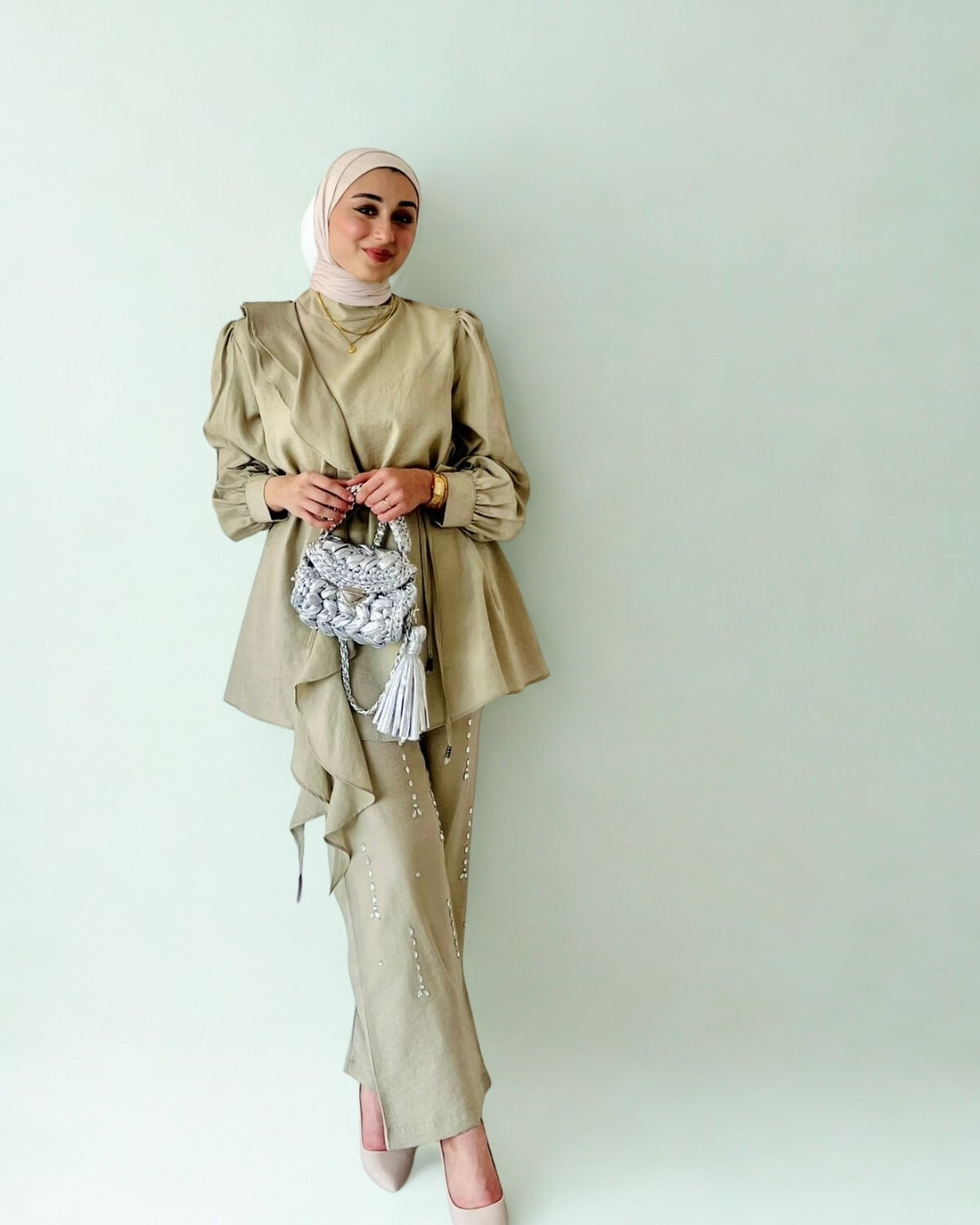 Woman wearing a beige traditional outfit with a headscarf against a light background