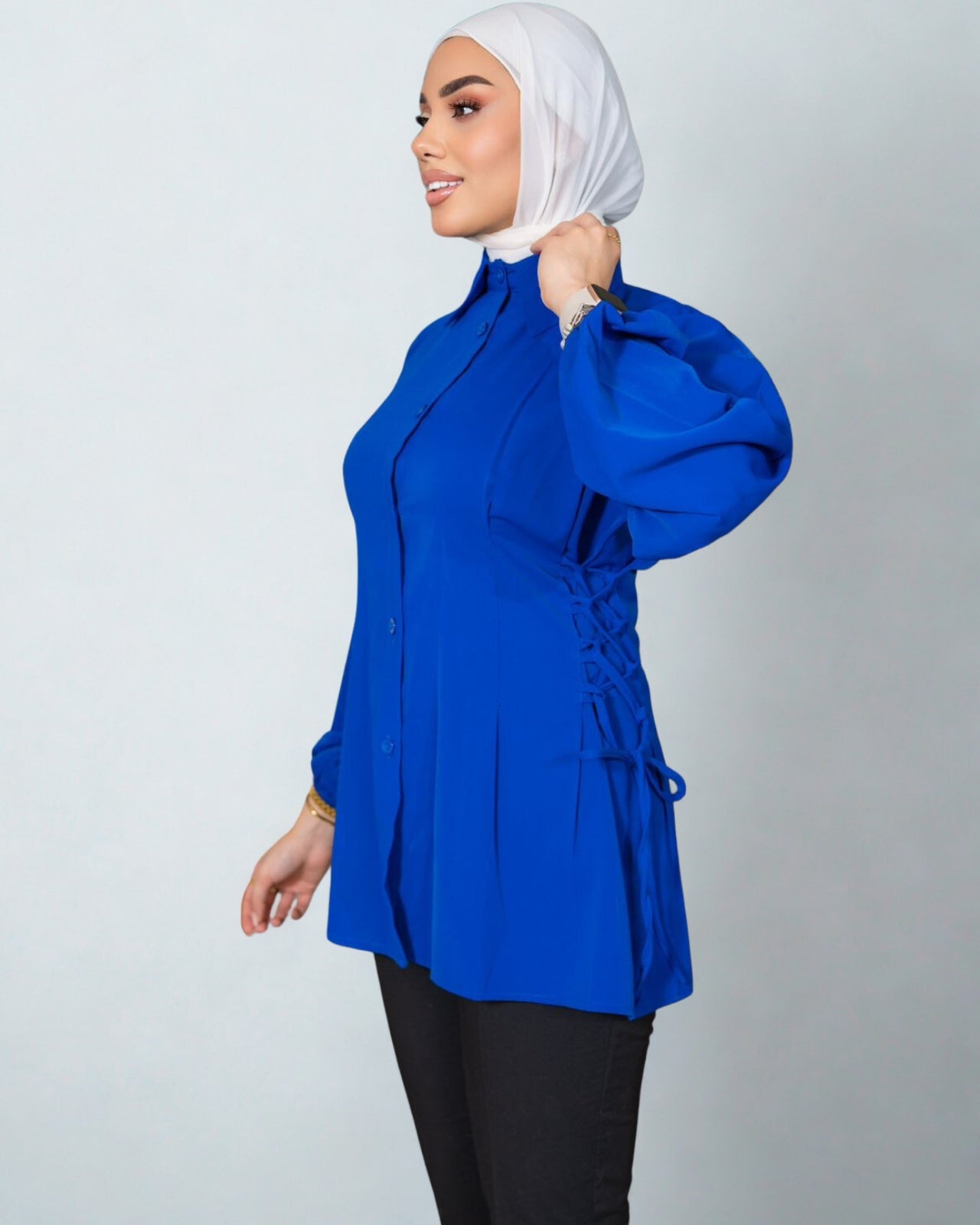 Woman wearing a blue top with a white hijab on a plain background