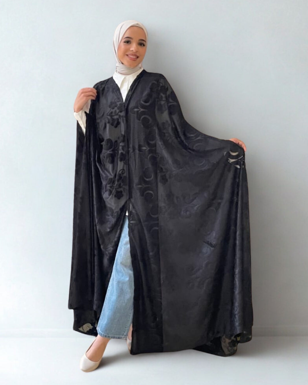 Woman holding a black abaya with floral embroidery on a plain background