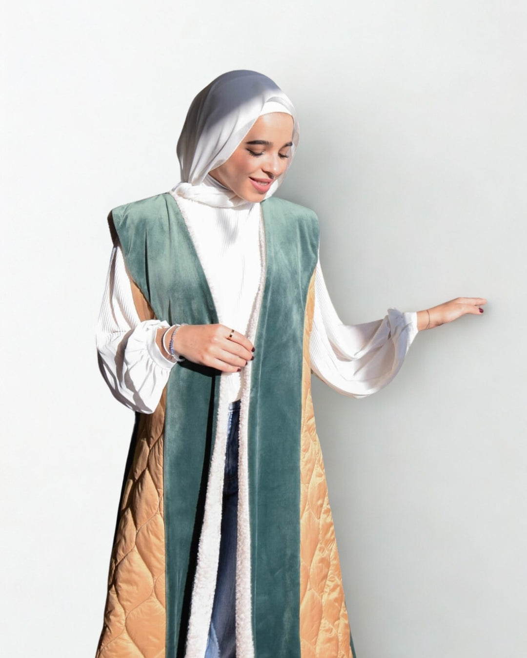 Woman wearing a green and beige abaya with a white hijab on a light gray background