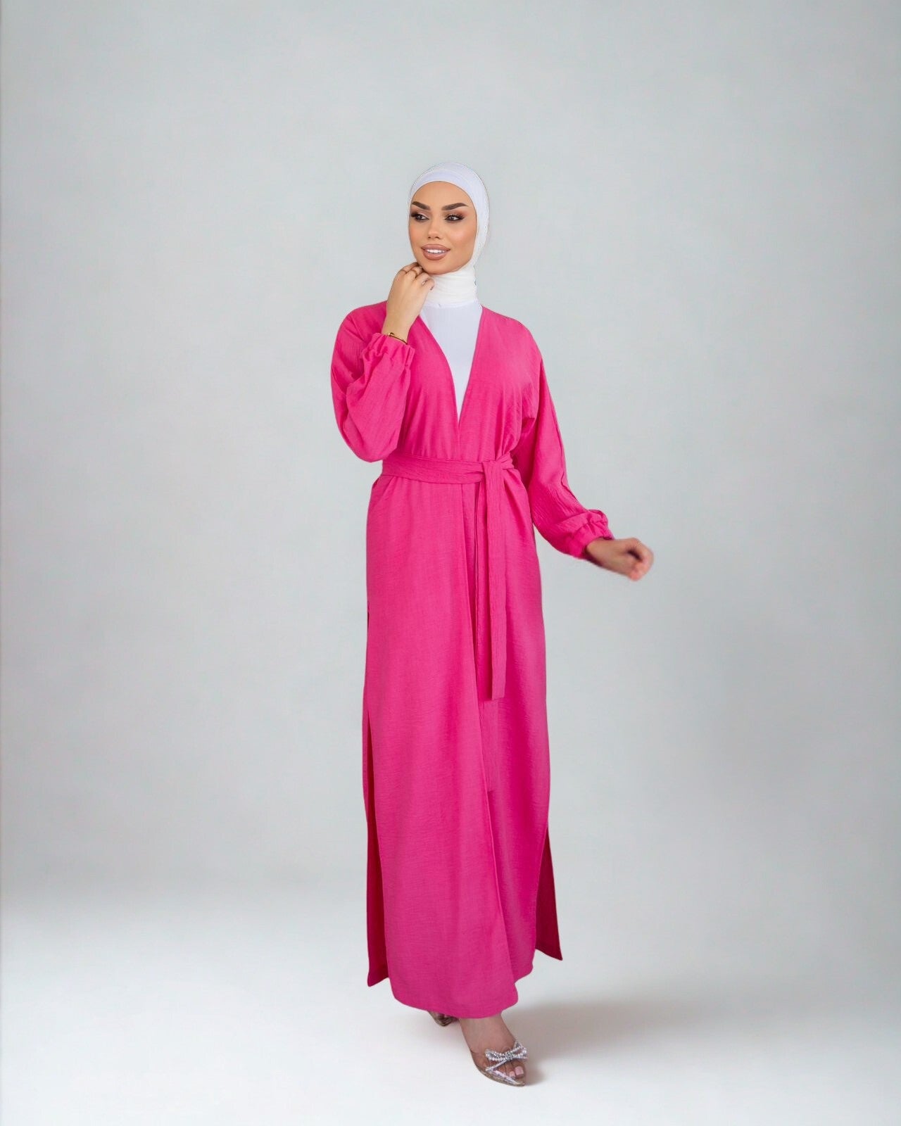 Woman wearing a bright pink dress with a white hijab on a light gray background