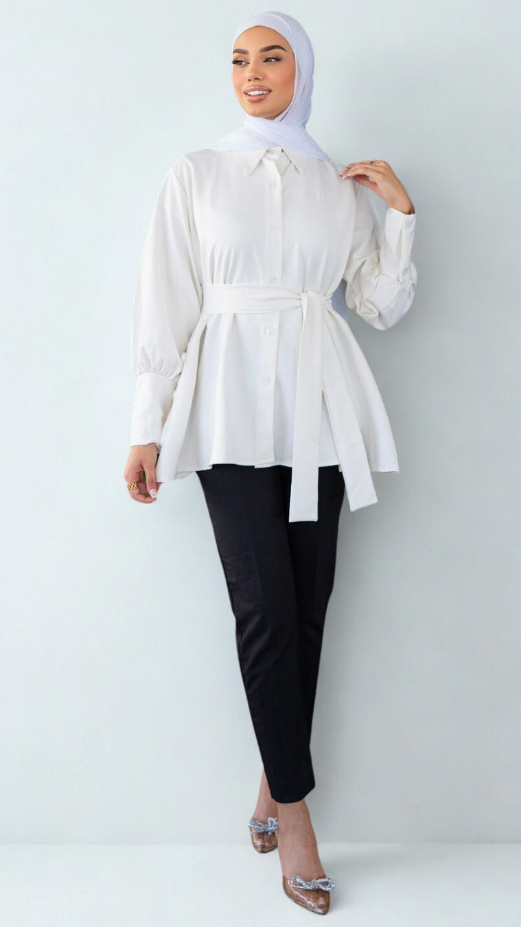 Woman wearing a white blouse and black pants with a hijab on a light gray background