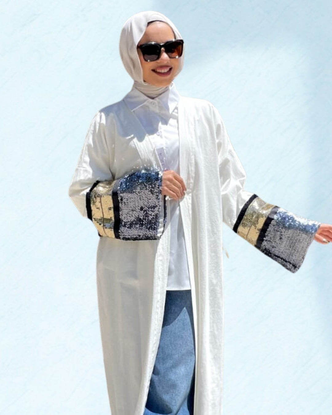 Woman wearing a white outfit with embellished sleeves against a light blue background