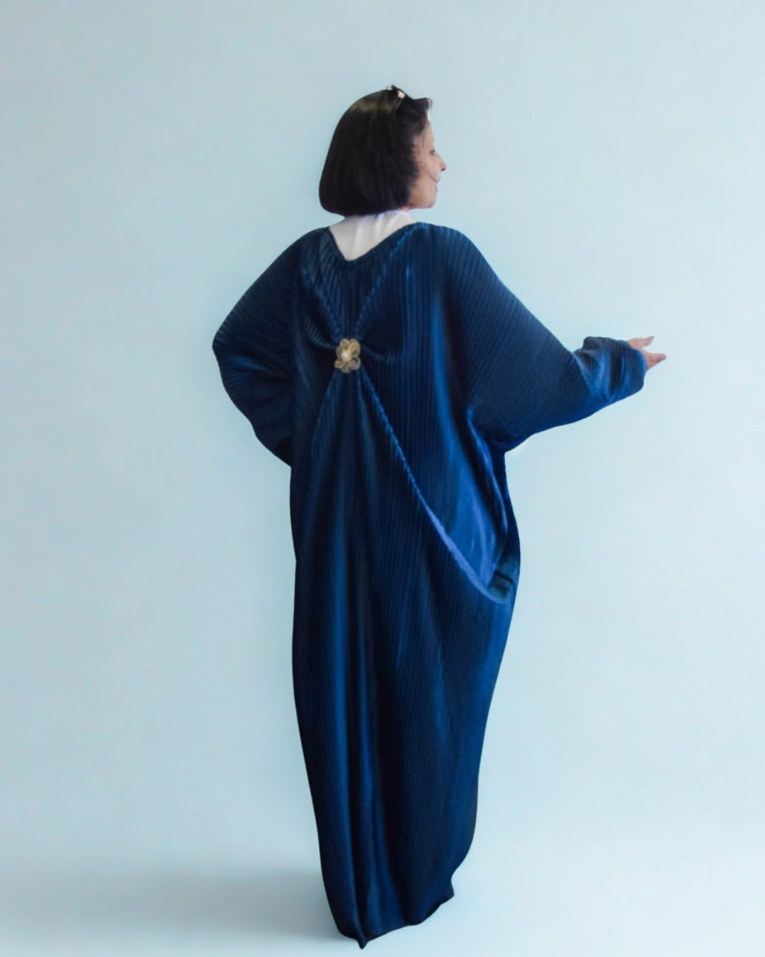 Woman wearing a blue velvet dress with a brooch on a light gray background