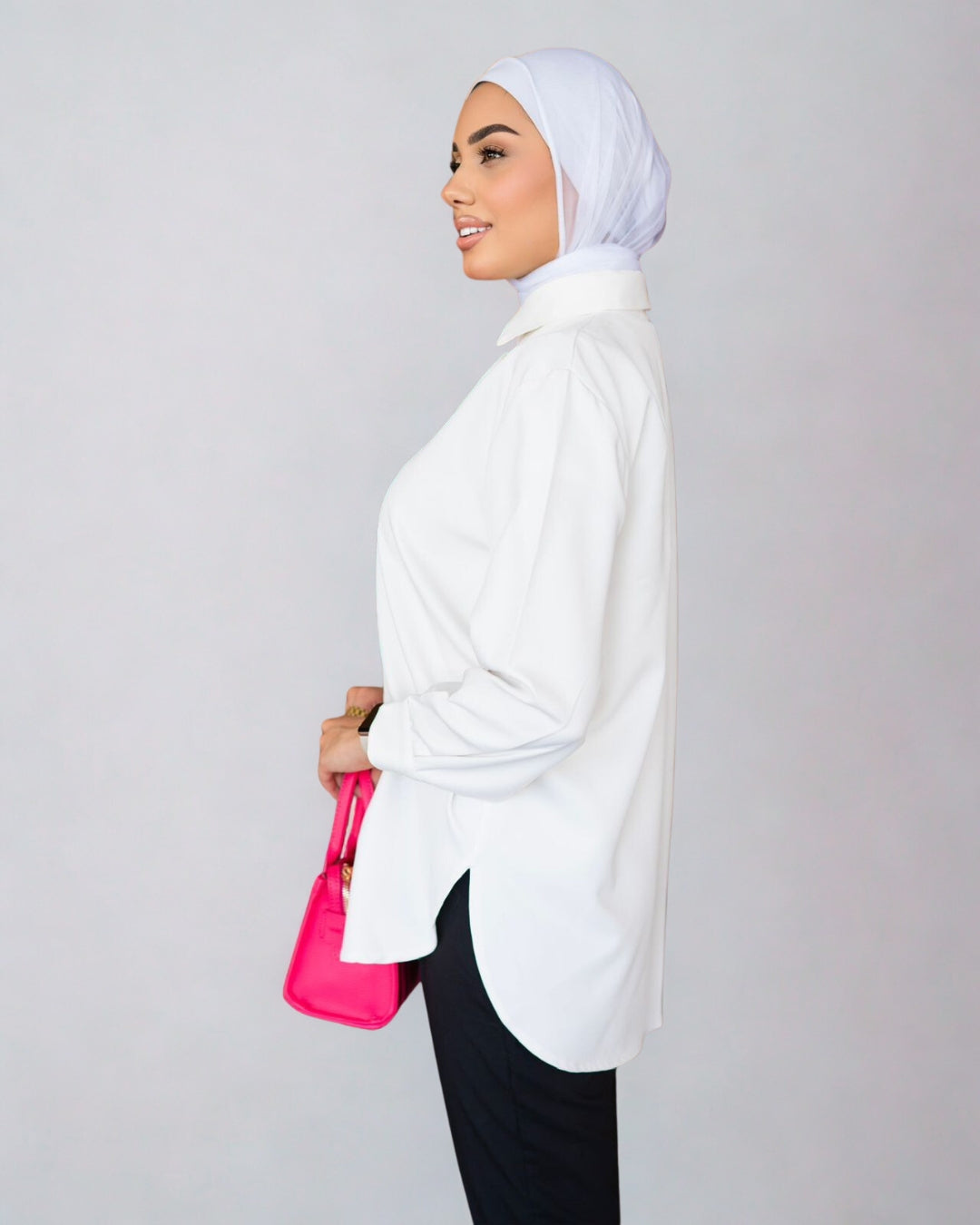 Woman wearing a white hijab and holding a pink bag against a gray background