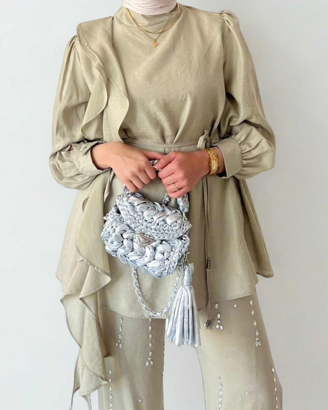 Person wearing a beige outfit with a textured handbag on a plain background