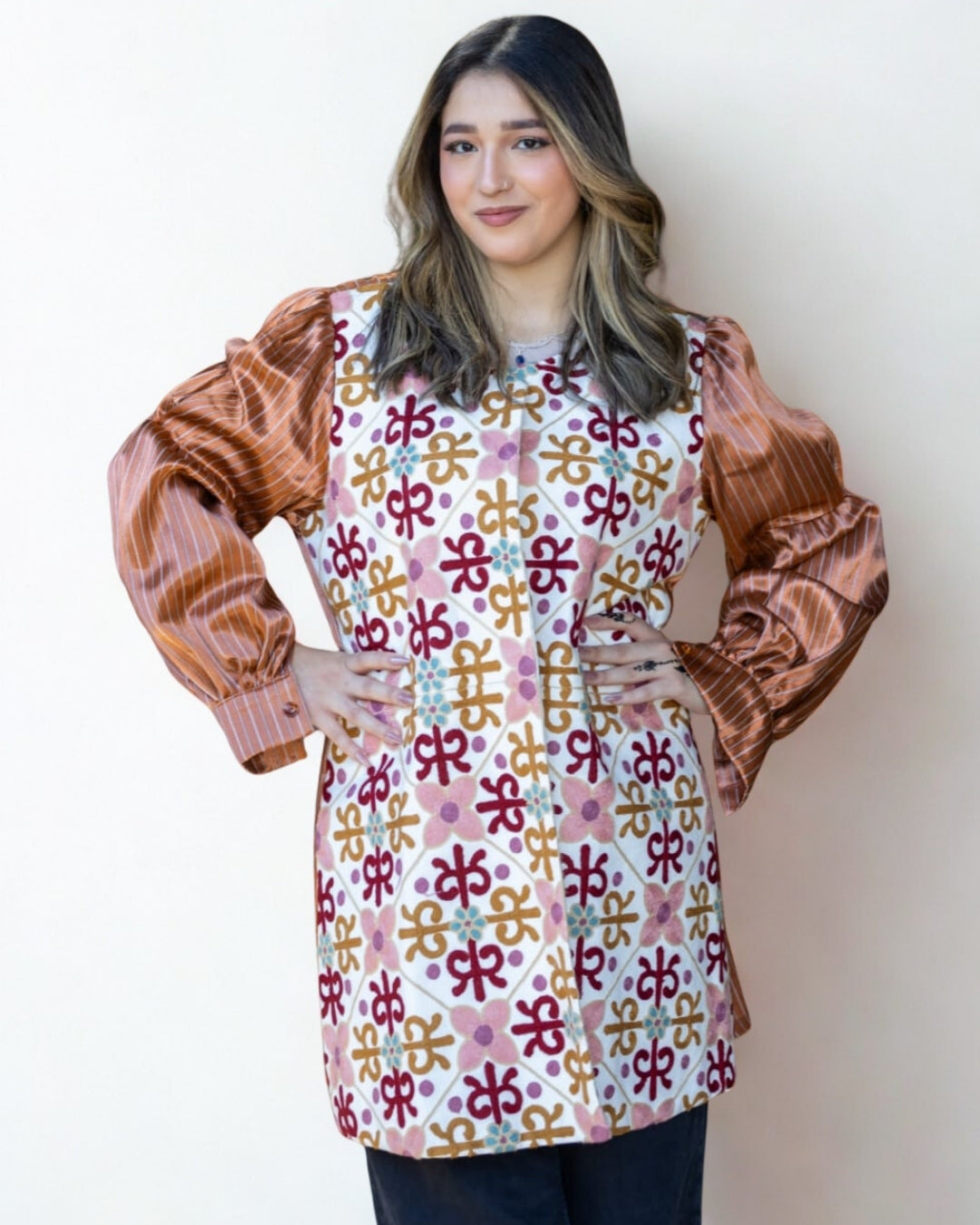 Woman wearing a colorful patterned blouse with brown sleeves against a white background