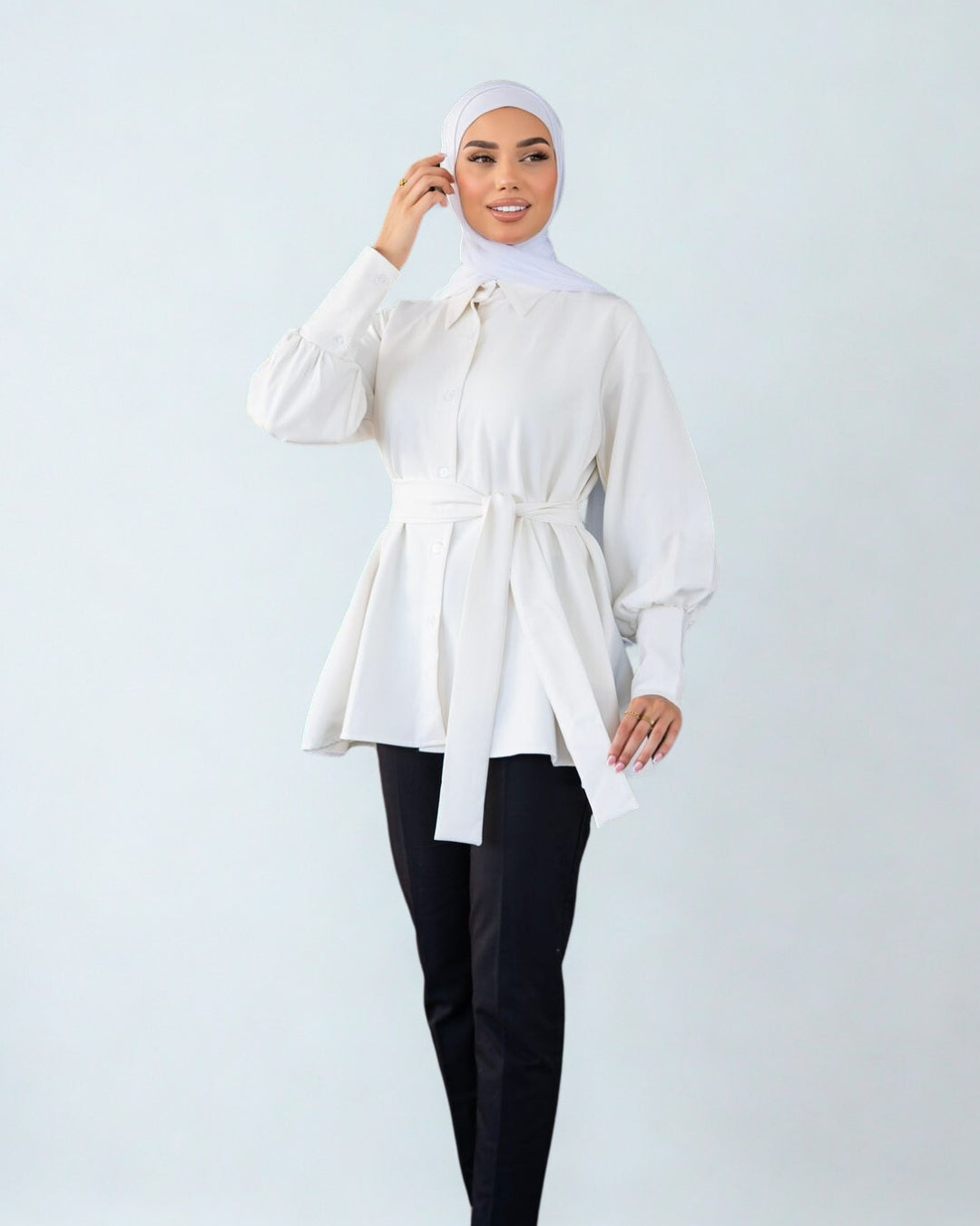 Woman wearing a white blouse with a belt and black pants on a light gray background