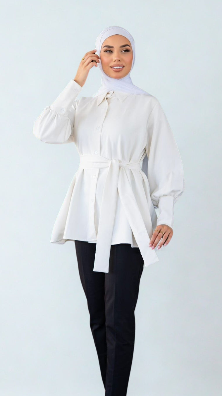 Woman wearing a white blouse with a belt and black pants on a light gray background