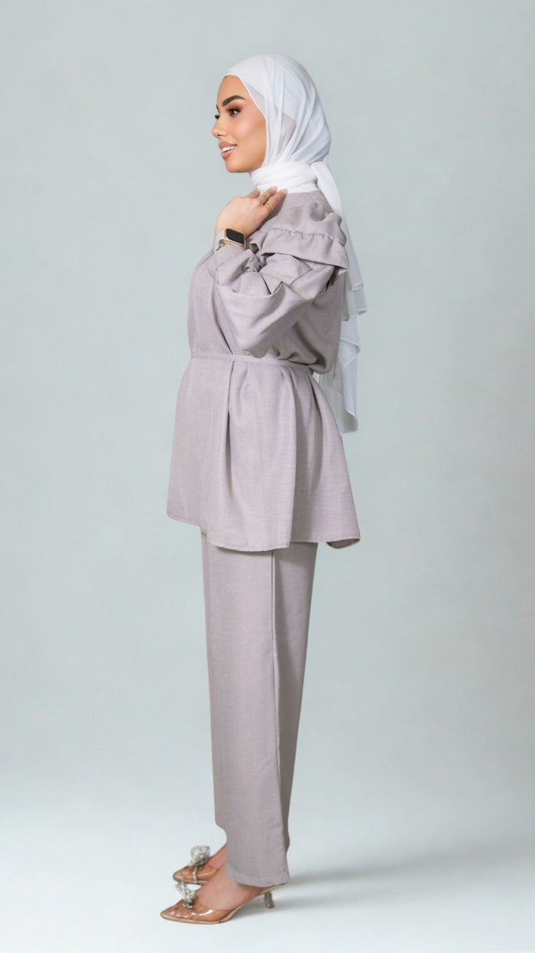 Woman wearing a light gray outfit with a matching hijab on a white background