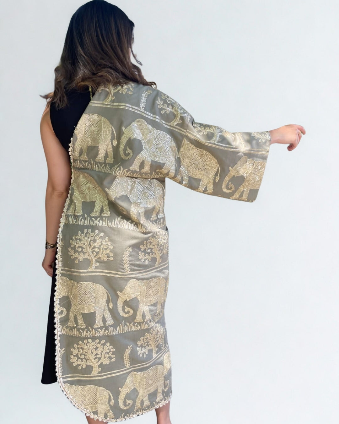 Woman wearing a long, patterned scarf with elephant designs on a plain background