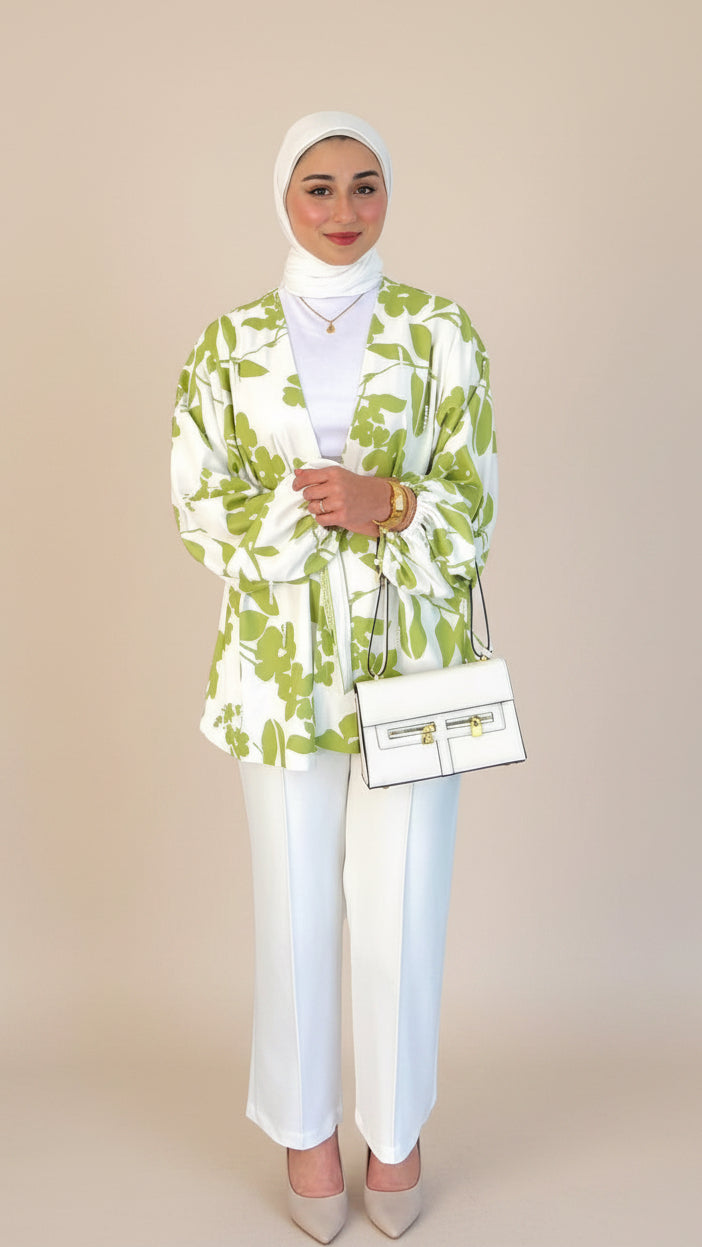 Woman wearing a green and white patterned blazer with white pants on a plain background