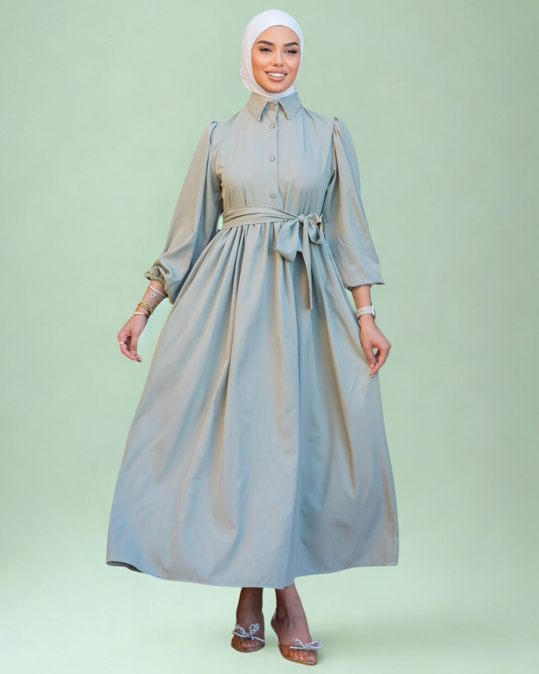 Woman wearing a long light gray dress with a belt on a light green background