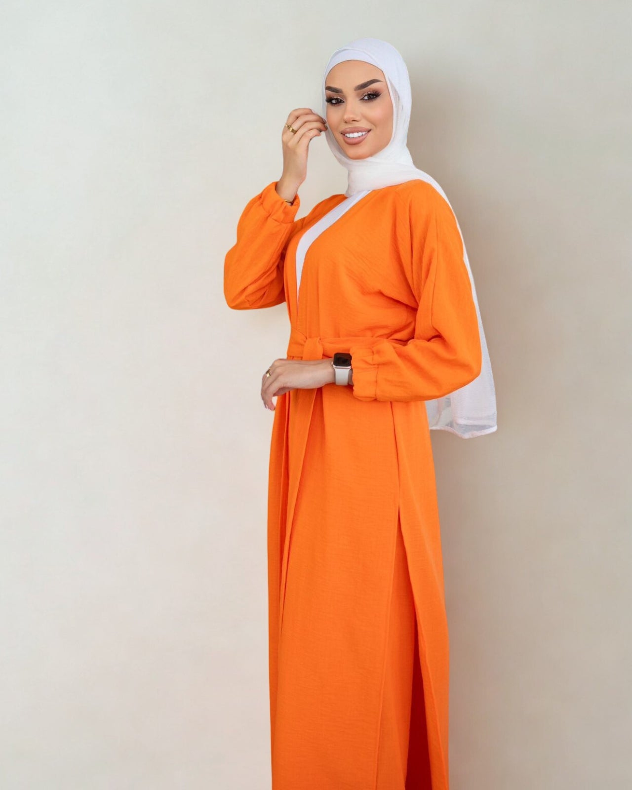 Woman wearing an orange dress with a white hijab on a plain background