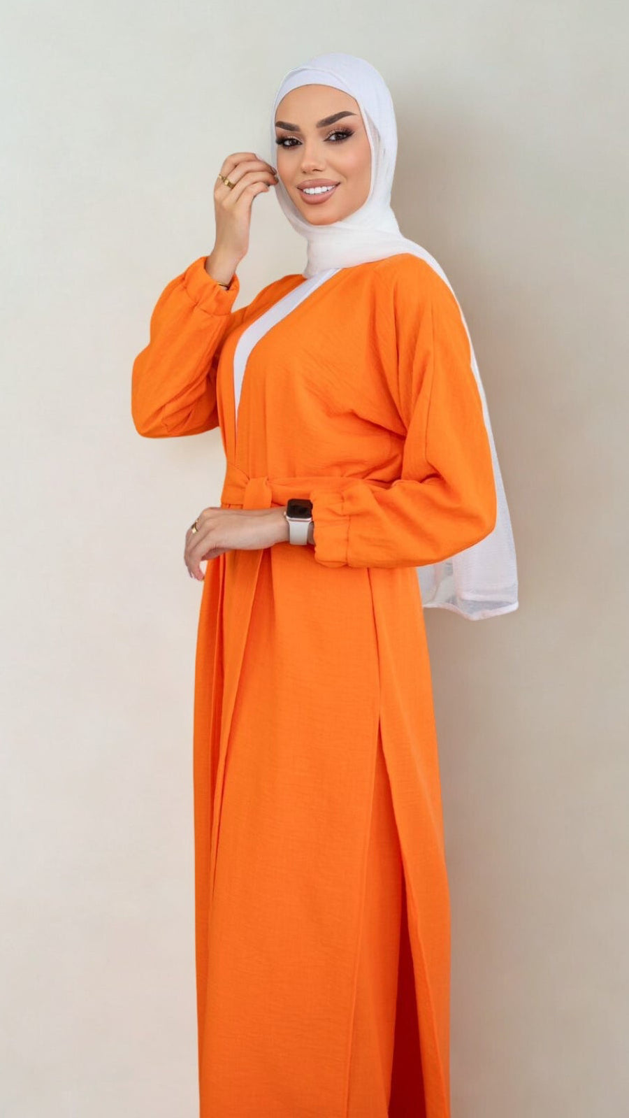 Woman wearing an orange dress with a white hijab on a plain background