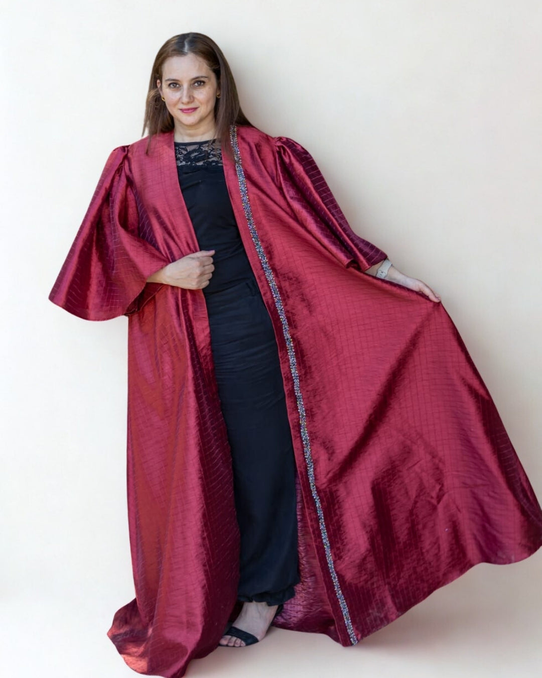 Woman wearing a long red robe over a black outfit against a white background