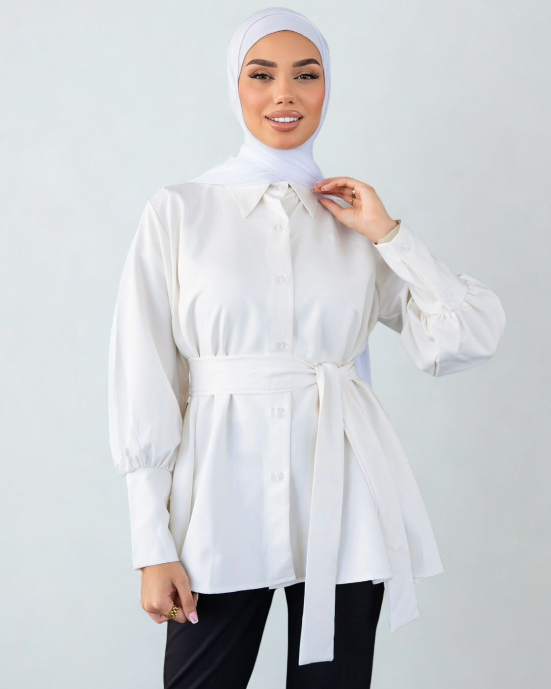 Woman wearing a white blouse with a belt and hijab on a plain background