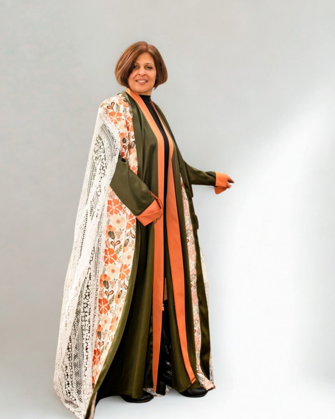 Woman wearing a long, dark green dress with floral patterns and orange accents on a white background