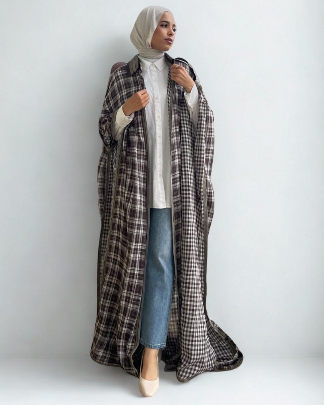 Person wearing a long plaid coat over a white shirt and blue jeans on a plain background