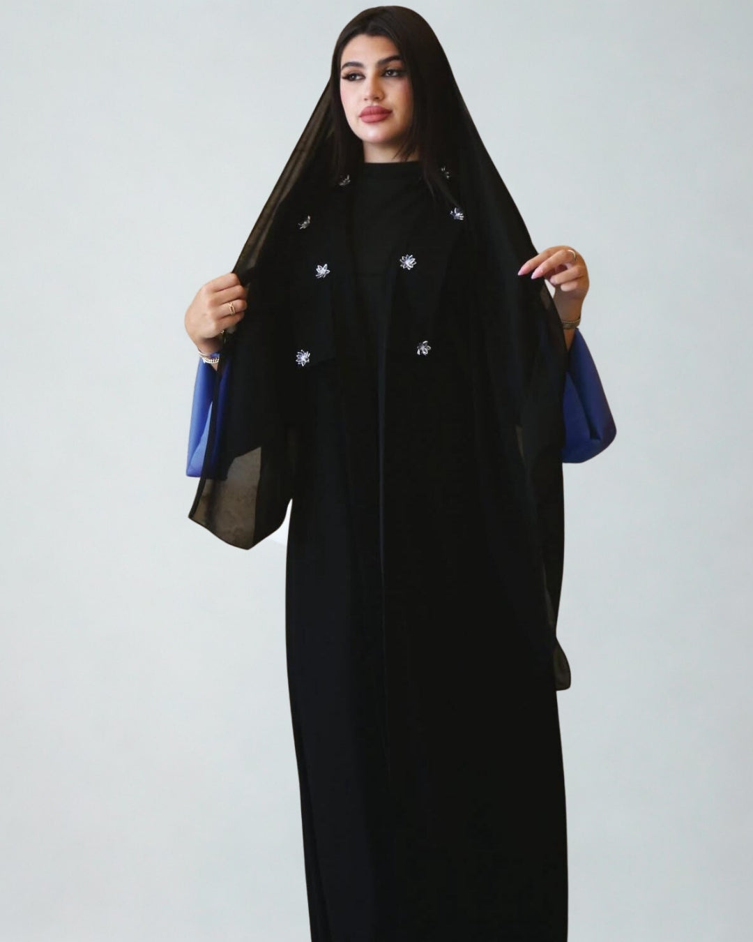 Woman wearing a black abaya with blue accents on a white background