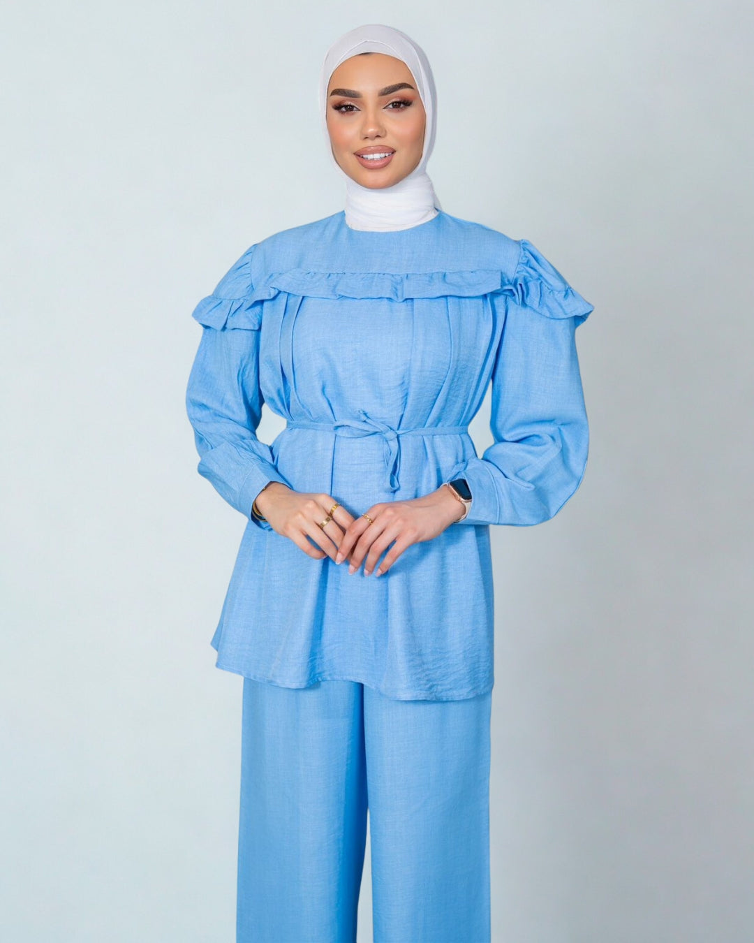Woman wearing a light blue outfit with a matching hijab on a plain background